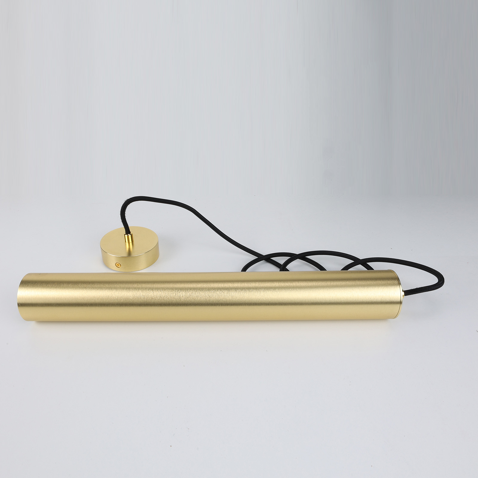 Una lámpara colgante cilíndrica de color dorado se encuentra horizontalmente. Tiene un cable negro adjunto.