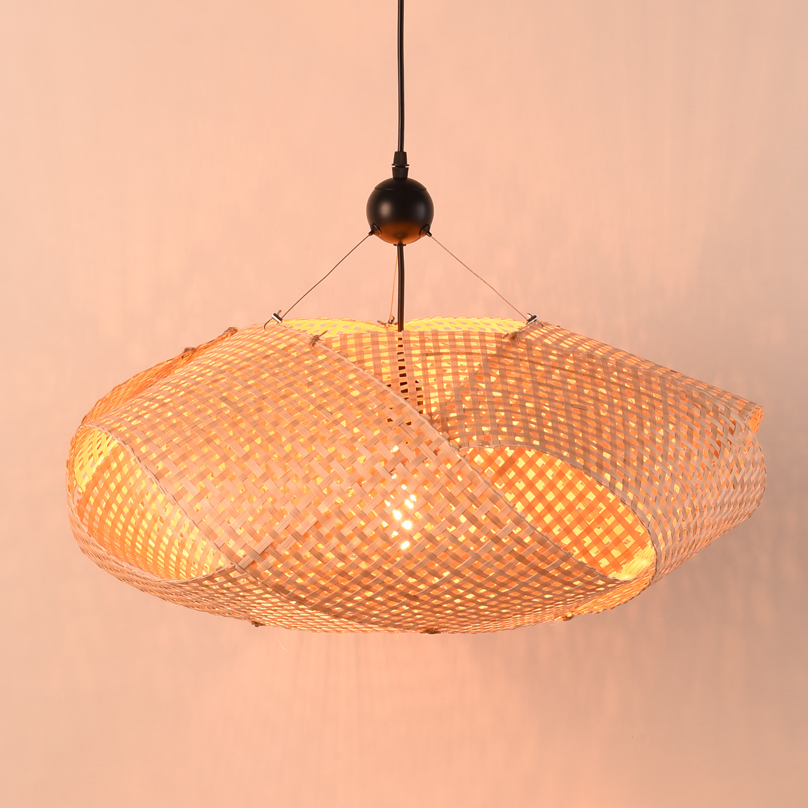 Una lámpara colgante de bambú tejido cuelga. La luz está encendida, iluminando el patrón tejido.