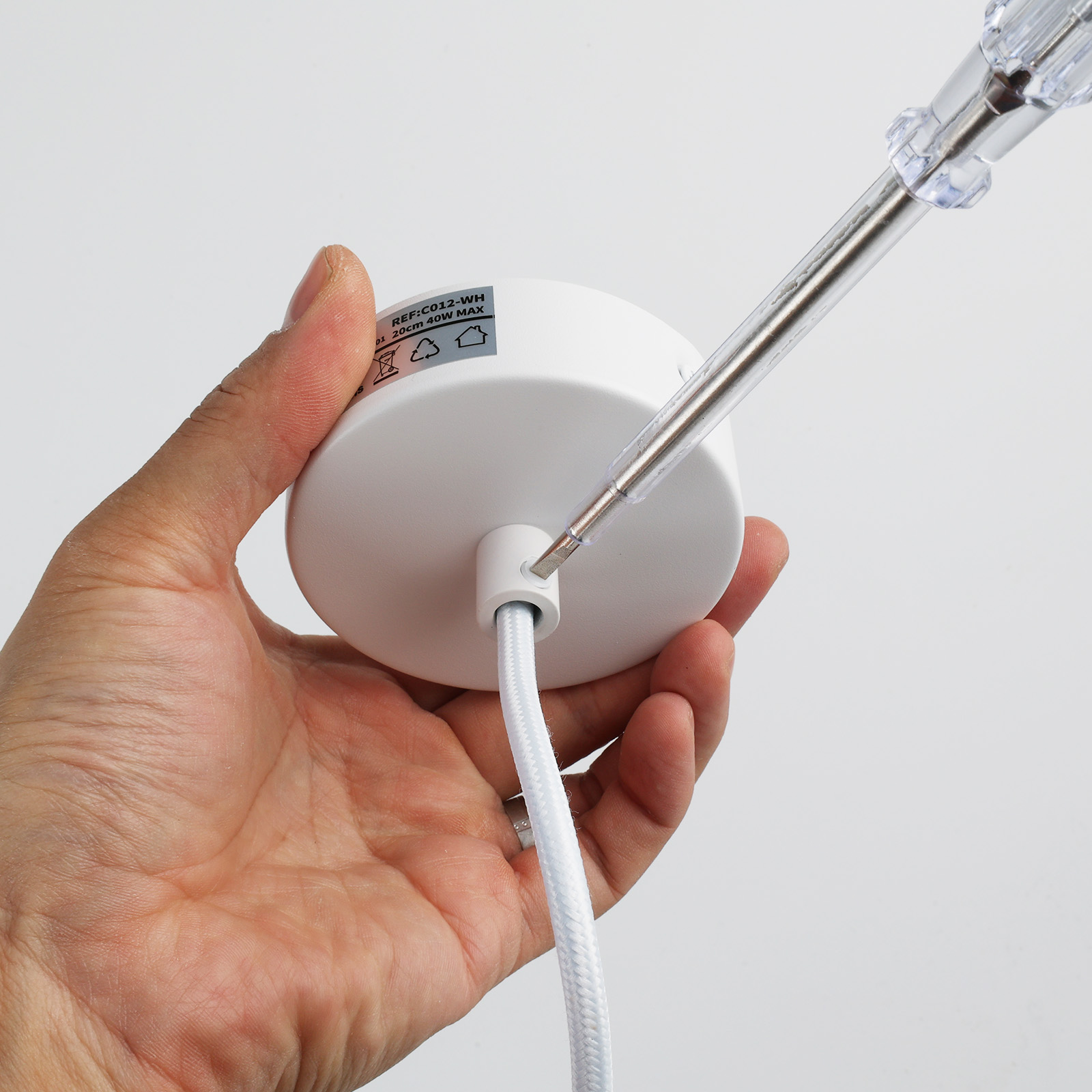 Una mano sosteniendo un accesorio de techo blanco. Se inserta un destornillador.
