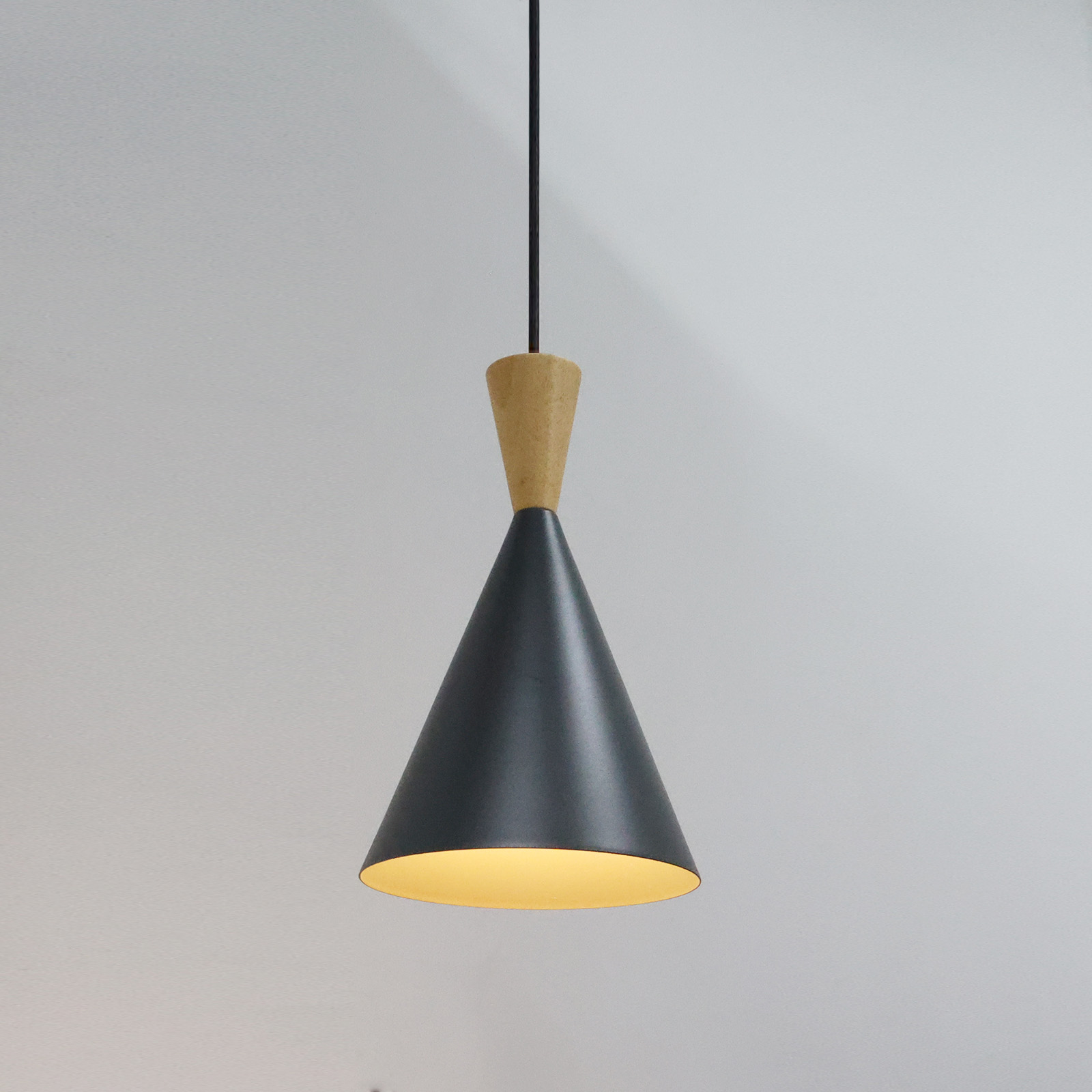 Una lámpara cónica con parte superior de madera y pantalla gris oscuro, iluminada desde dentro.