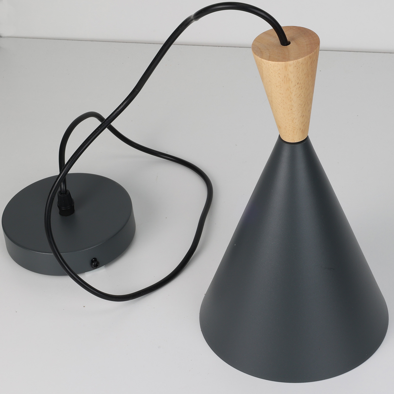 Primer plano de una lámpara colgante negra. La parte superior es de madera y la base en forma de cono es gris oscuro. El cable es negro.