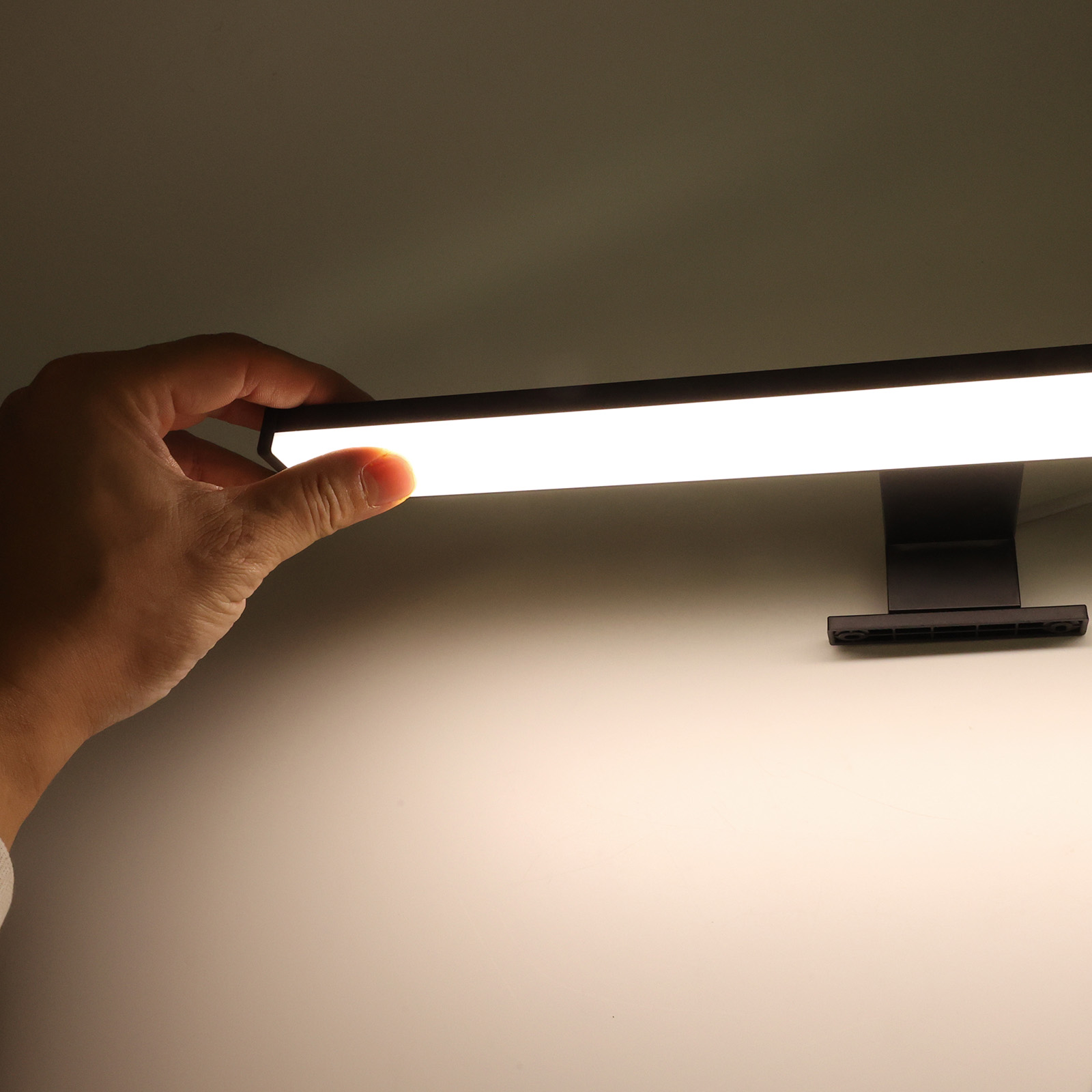 Una mano está tocando una luz de tocador. La luz está encendida. El fondo es blanco.