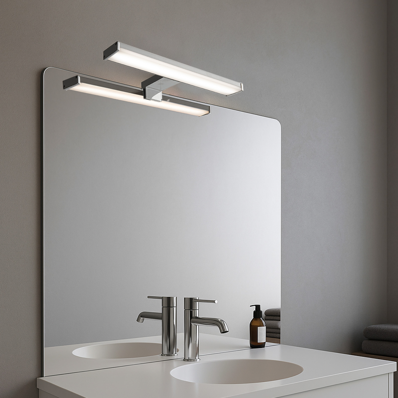 Dos luces de tocador están montadas encima de un lavabo y un espejo. También hay un grifo y artículos de tocador. Fondo gris.