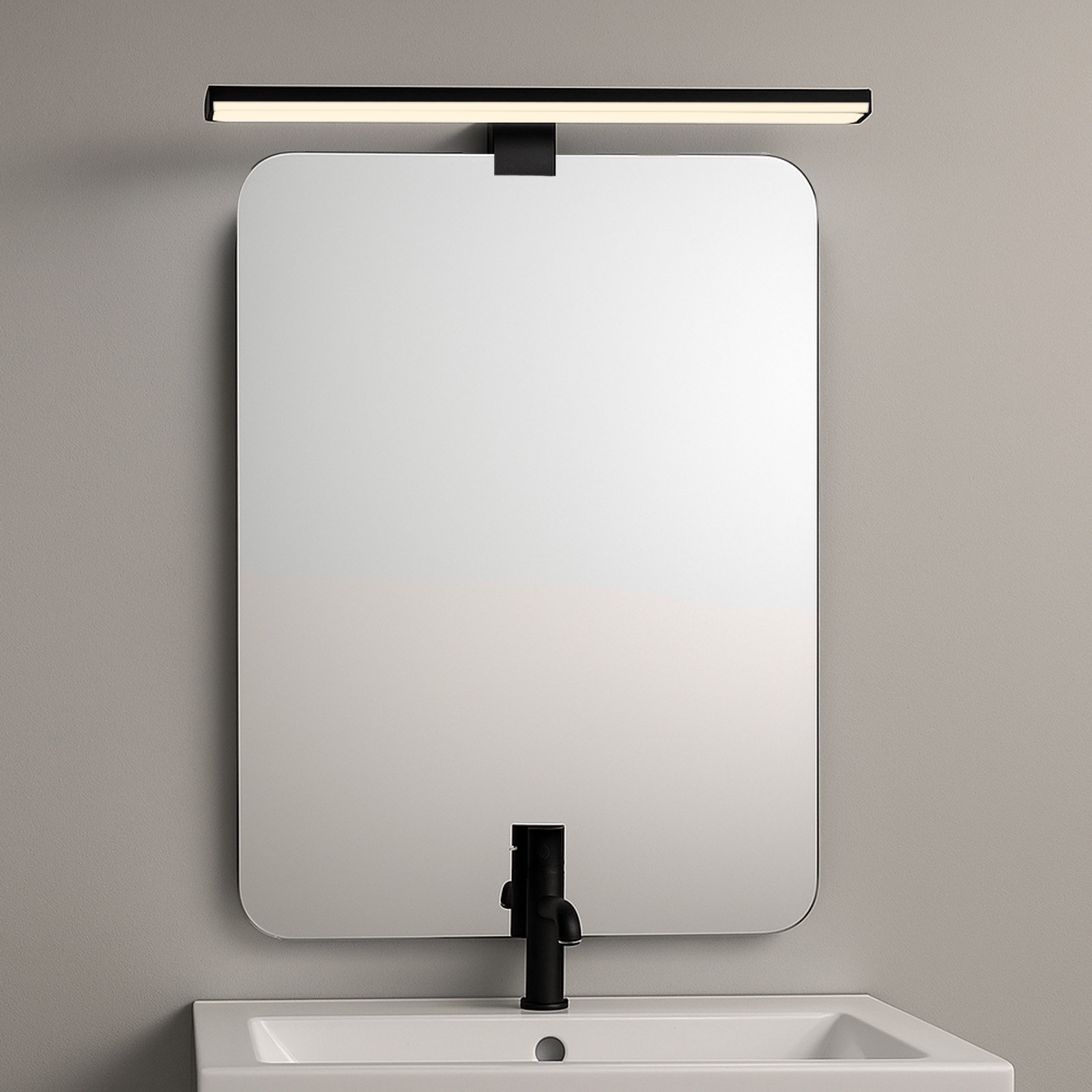 Una luz de tocador negra está encima de un espejo. Un grifo negro y un lavabo están debajo. El fondo es gris.