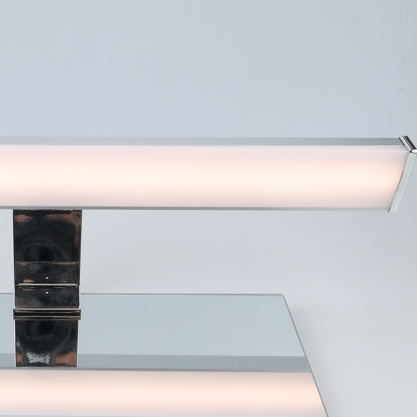 Primer plano de una luz de tocador montada encima de un espejo. La luz es plateada y rectangular, y el fondo es blanco.