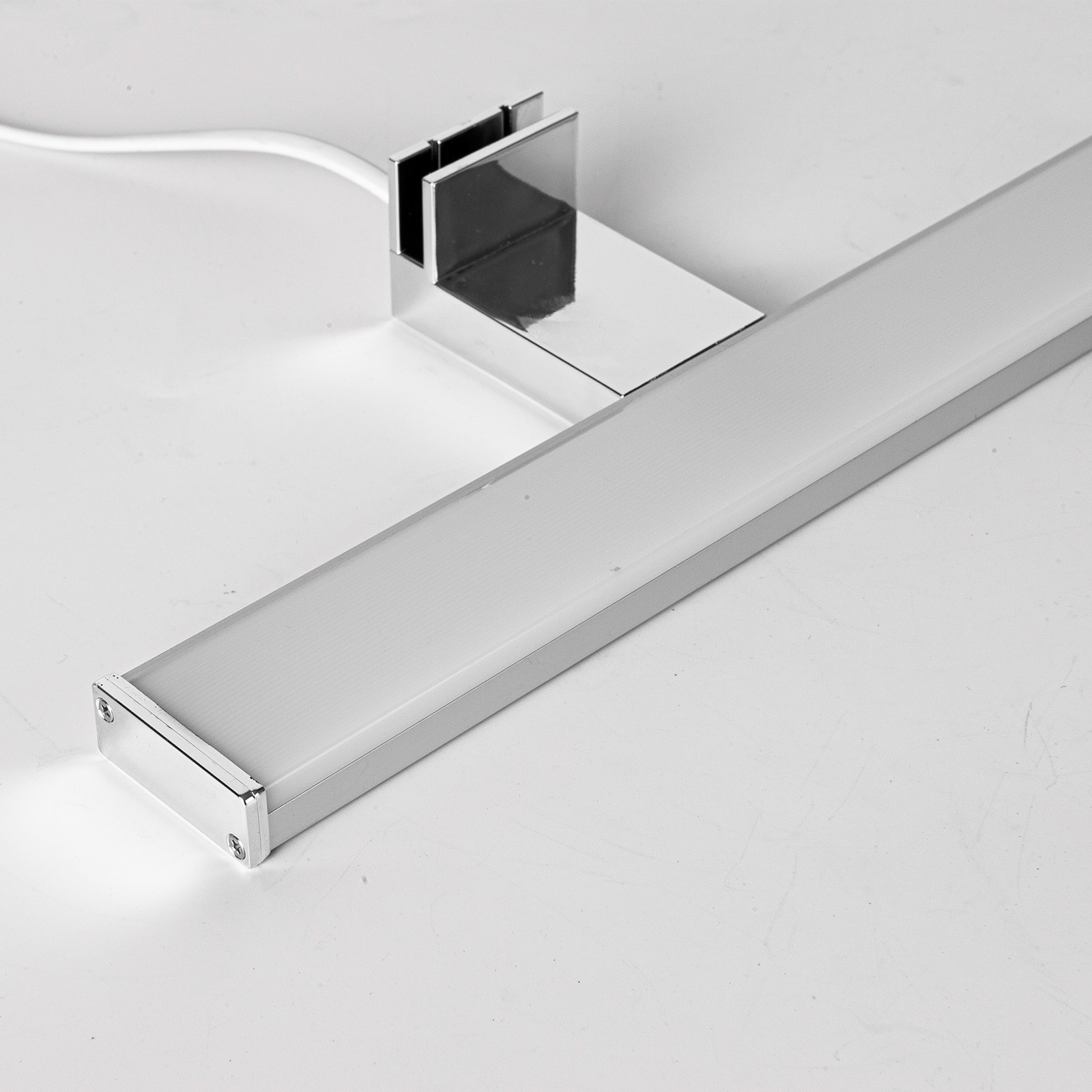 Primer plano de una lámpara LED plateada sobre una superficie blanca. La lámpara tiene luz blanca y base metálica.