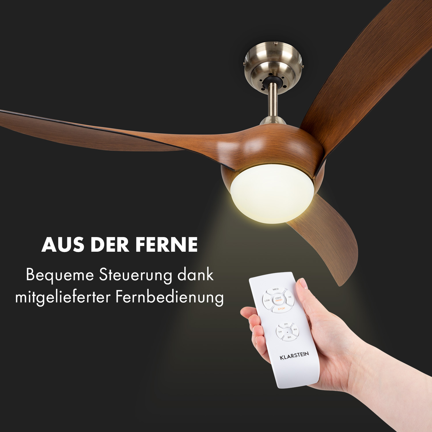 Una mano che tiene un telecomando per un ventilatore da soffitto con pale in legno, su sfondo nero.