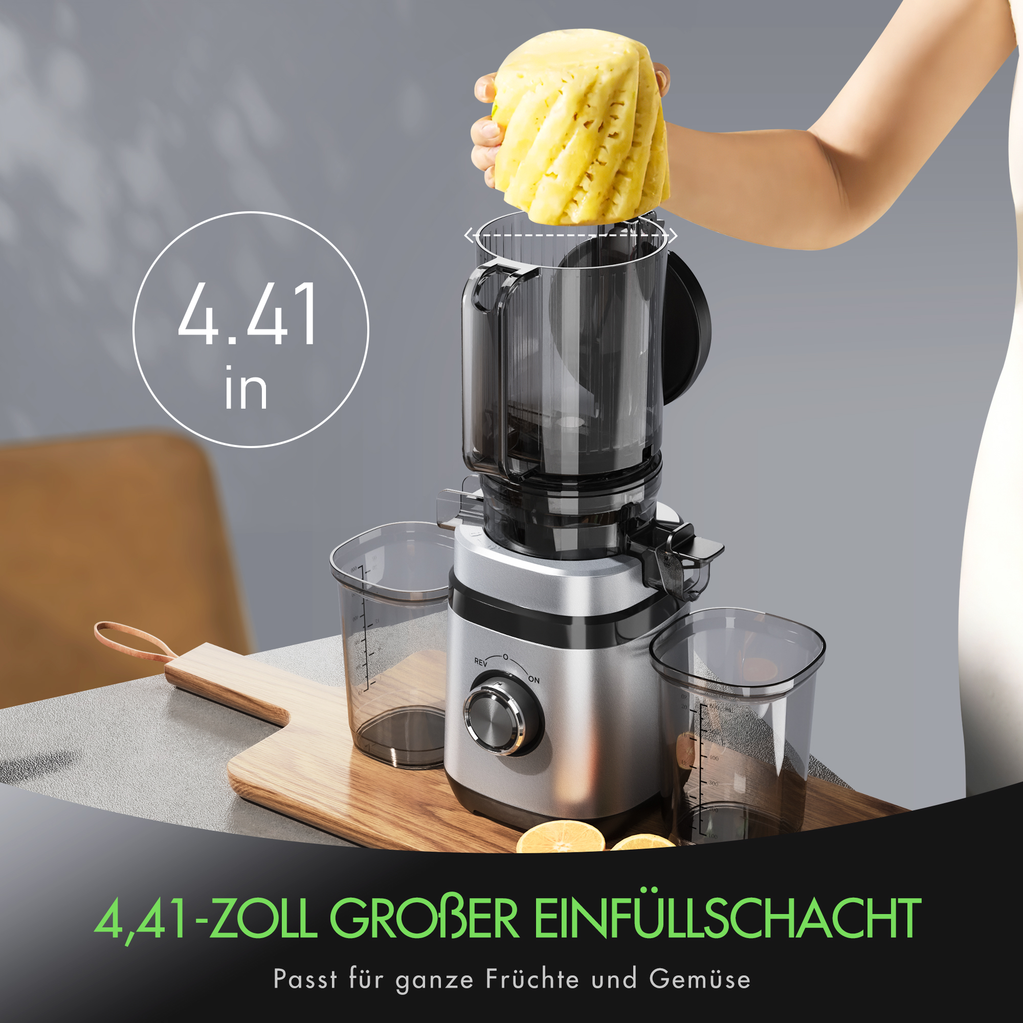 Eine Person legt ein Ananasstück in einen Entsafter. Der Entsafter ist silberfarben mit schwarzen Teilen. Auf jeder Seite befindet sich ein Messbecher.