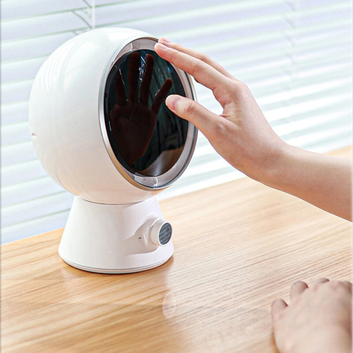 Dispositivo blanco de forma ovalada con una mano delante, mostrando una silueta. El dispositivo está sobre una mesa de madera.