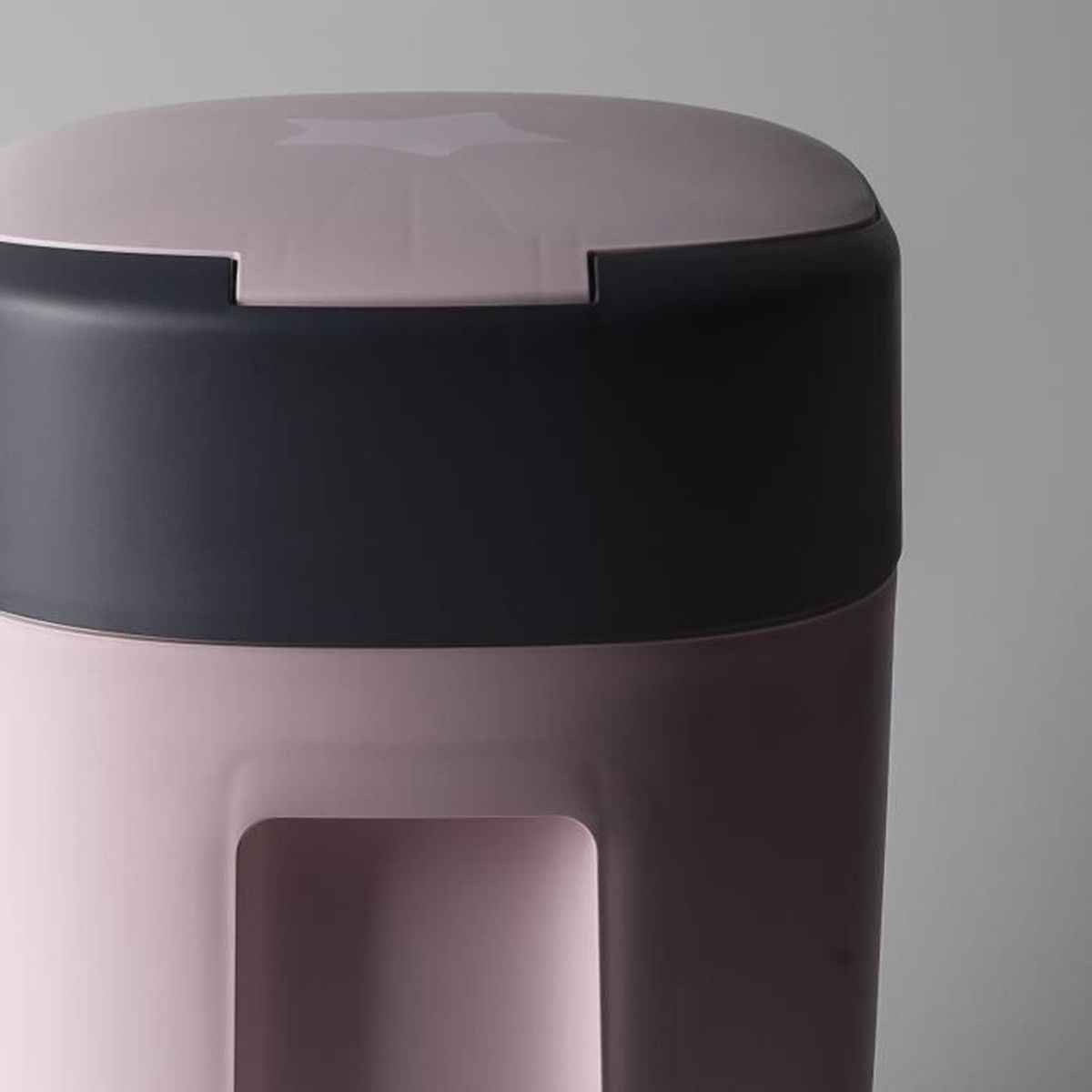 Ein rosa und grauer Windeleimer. Der Deckel ist grau, der Korpus rosa. Das Design ist stromlinienförmig und modern.