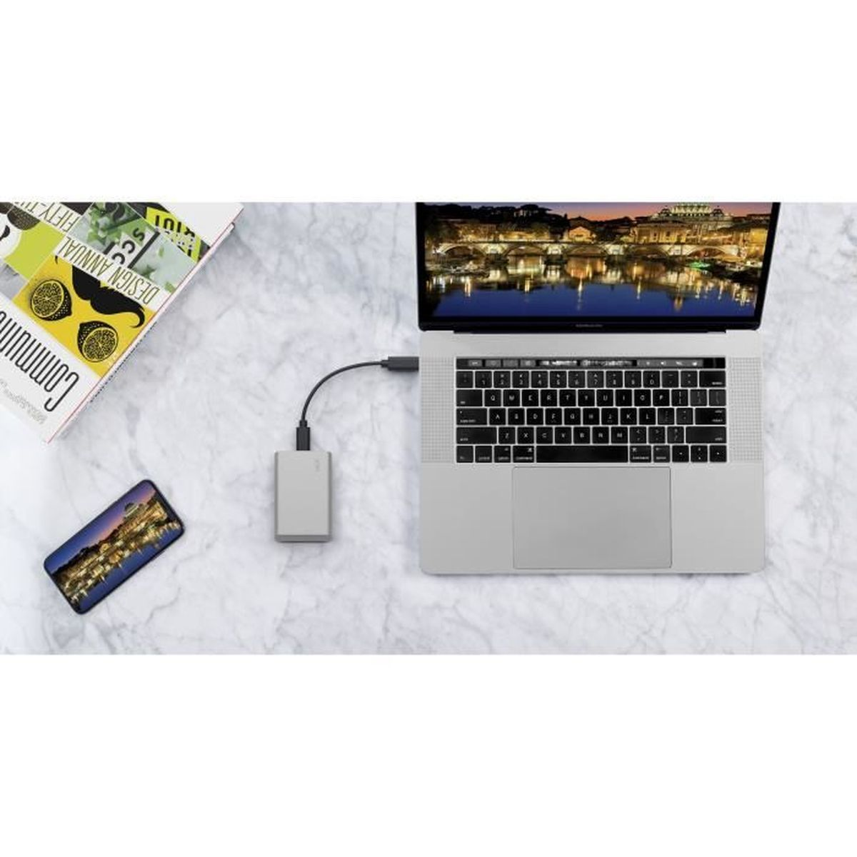 Ein Laptop mit Festplatte und Smartphone auf Marmor, im Hintergrund ein Magazin.