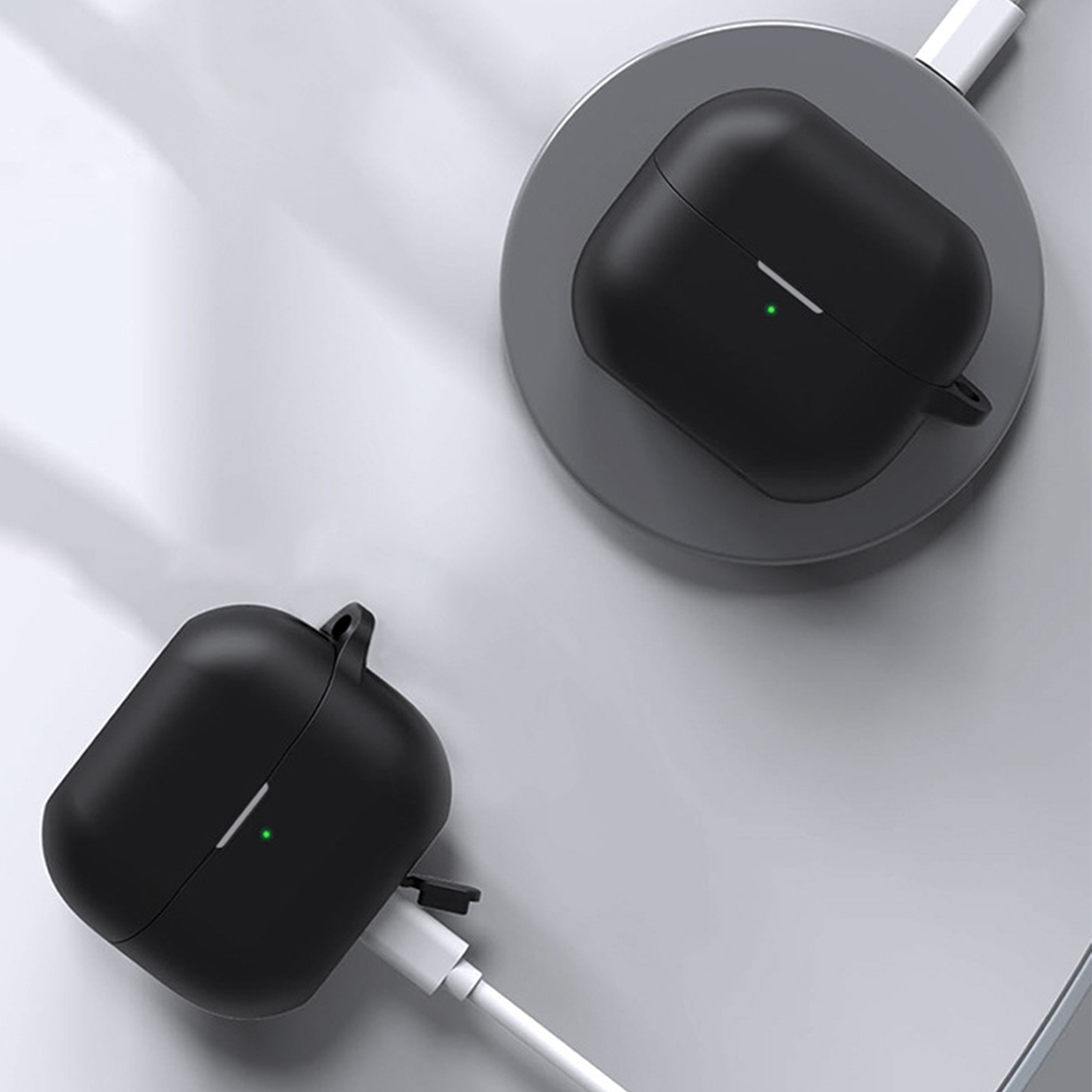 L'immagine mostra due custodie nere per auricolari wireless in carica su una superficie grigia con cavi bianchi.
