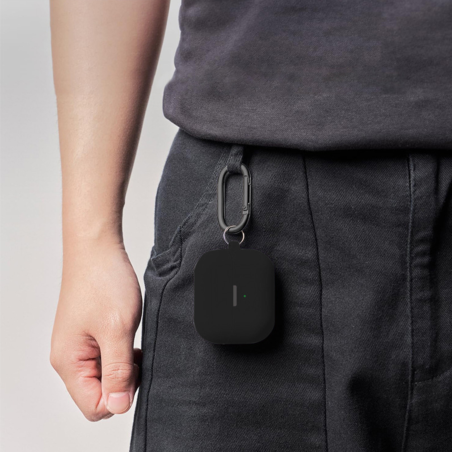 La mano di una persona che tiene una custodia nera per auricolari attaccata ai pantaloni. La custodia ha una luce verde.
