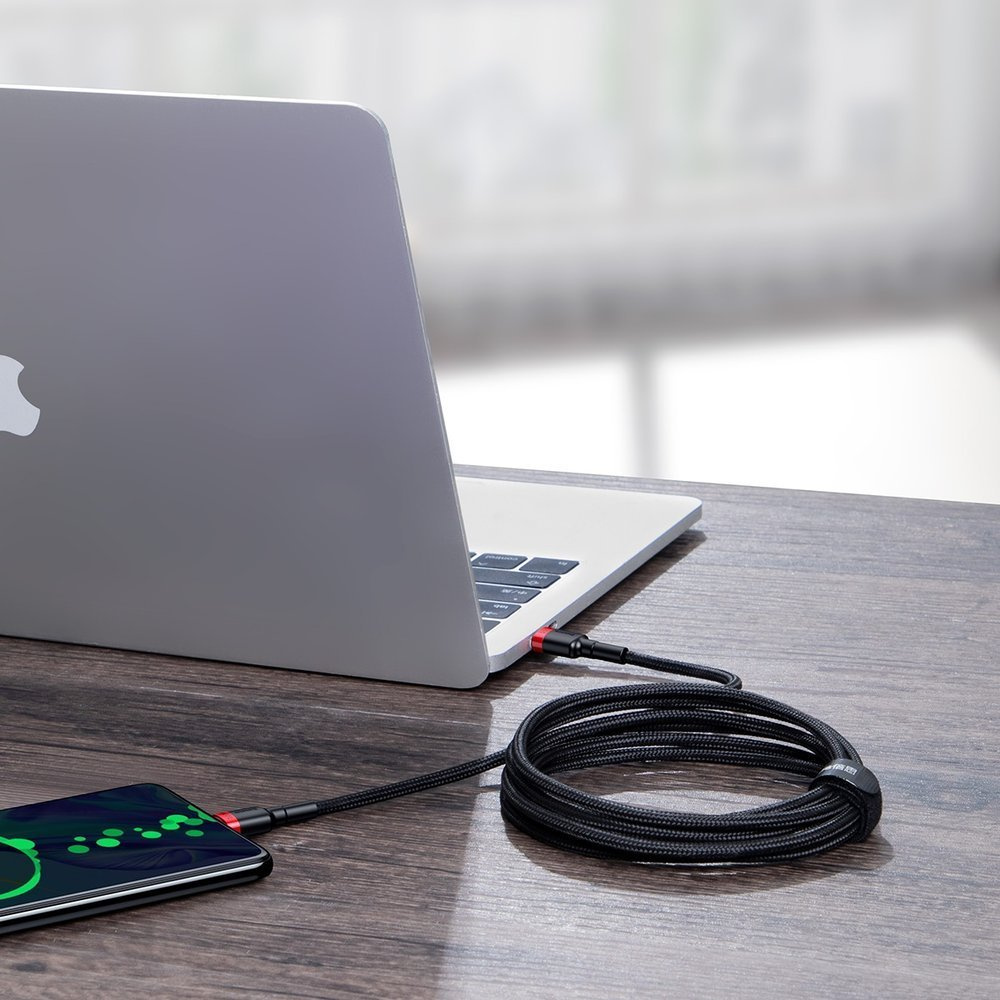 Laptop ładuje się czarnym kablem, podłączonym do telefonu na biurku.