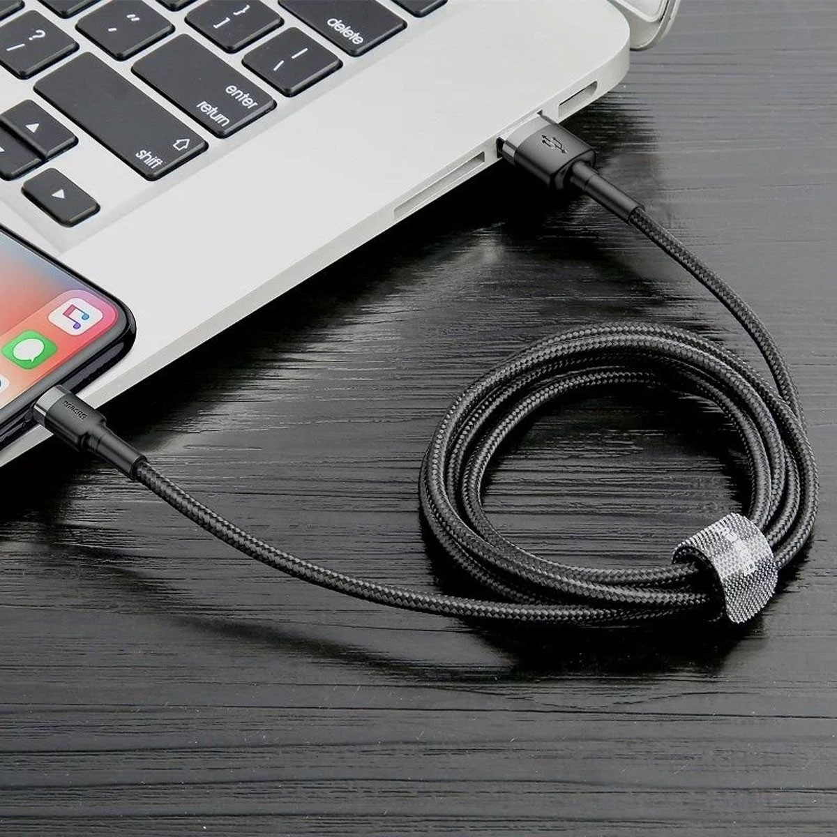 Czarny kabel USB do Lightning podłączony do laptopa i telefonu. Kabel jest pleciony i ma opaskę.