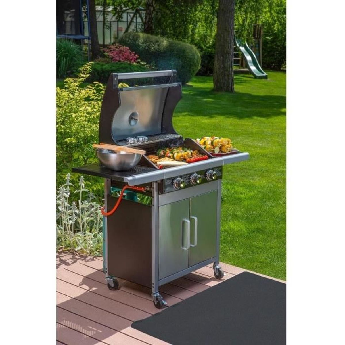 Ein Edelstahlgrill auf einem Holzdeck in einem Hinterhof mit Rutsche.