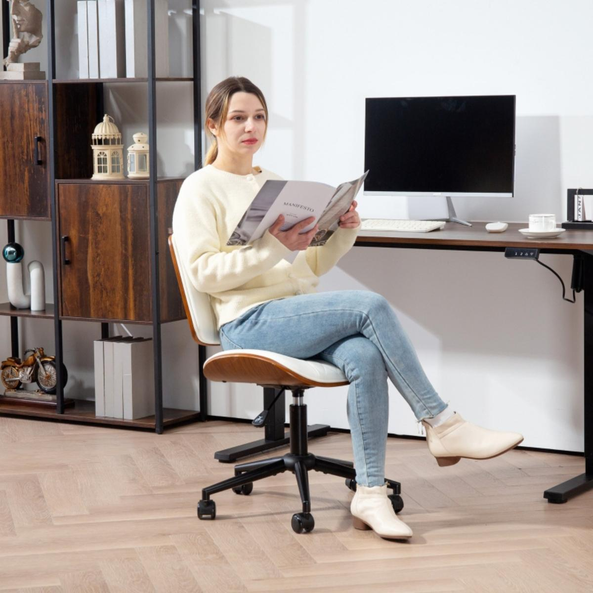 Eine Frau sitzt in einem Stuhl und liest ein Buch. Sie sitzt vor einem Schreibtisch mit Computer und anderen Gegenständen.
