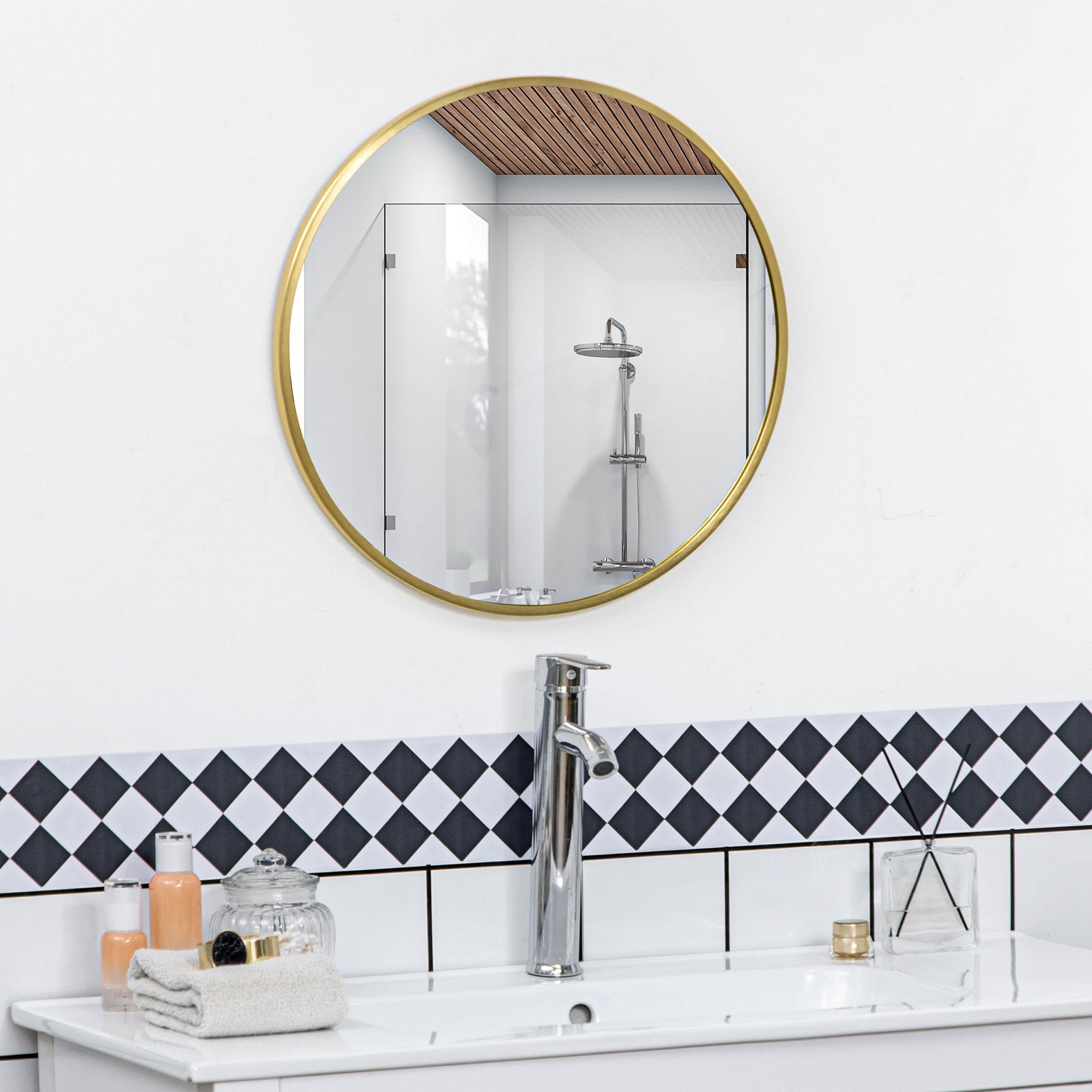 Badezimmer mit rundem, goldgerahmtem Spiegel, Waschbecken mit Wasserhahn und Toilettenartikeln. Schwarz-weiße Fliesen.