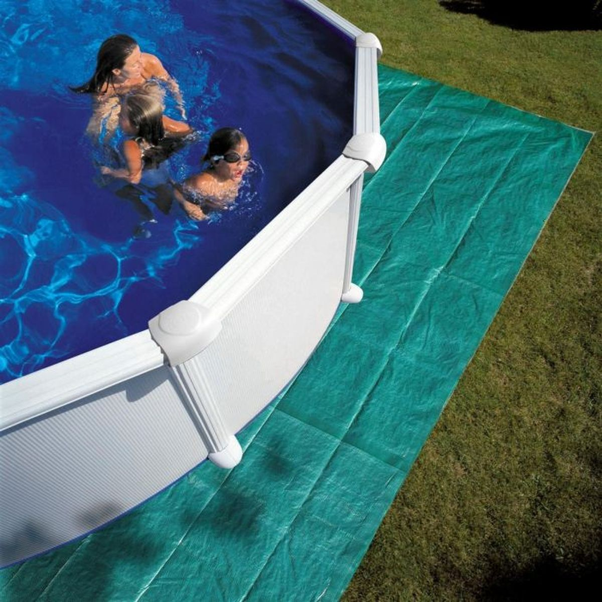 Una familia nada en una piscina. Una estera verde y hierba en primer plano.