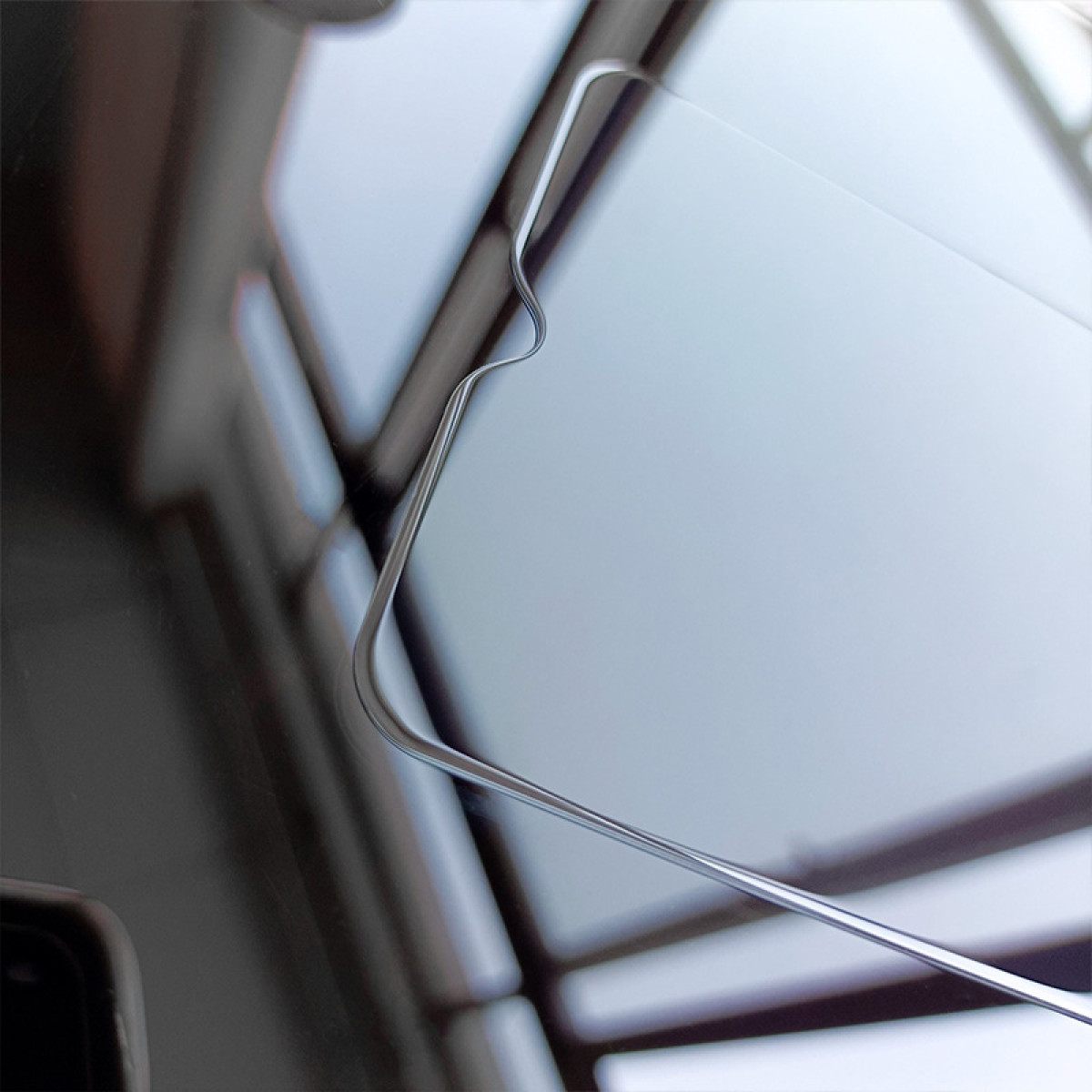 Nahaufnahme einer gekrümmten Bildschirmkante, die einen verschwommenen Raum reflektiert. Der Bildschirm scheint aus Glas zu sein.