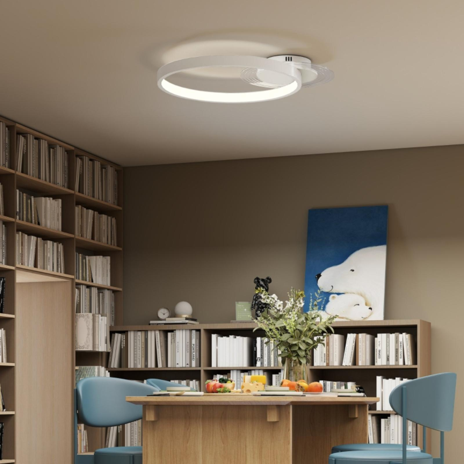 Eine moderne Deckenleuchte in einem Raum mit Bücherregalen, einem Tisch und Stühlen.