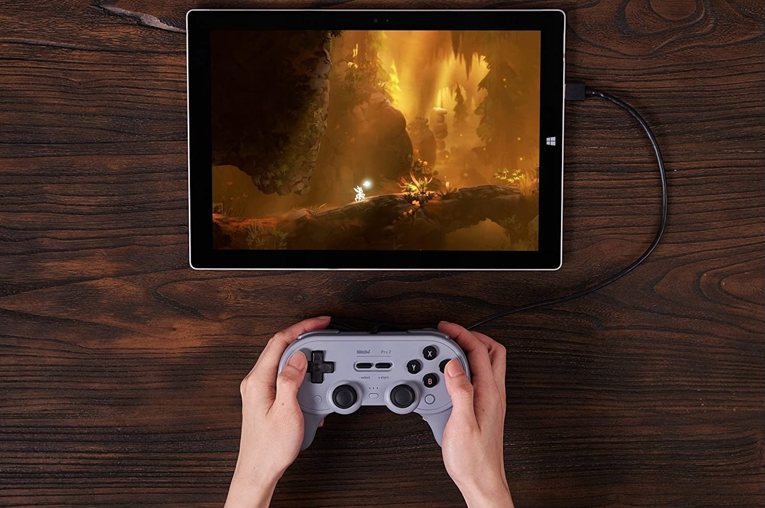 Hände halten grauen Controller, spielen Spiel auf Tablet. Holz Tisch im Hintergrund.