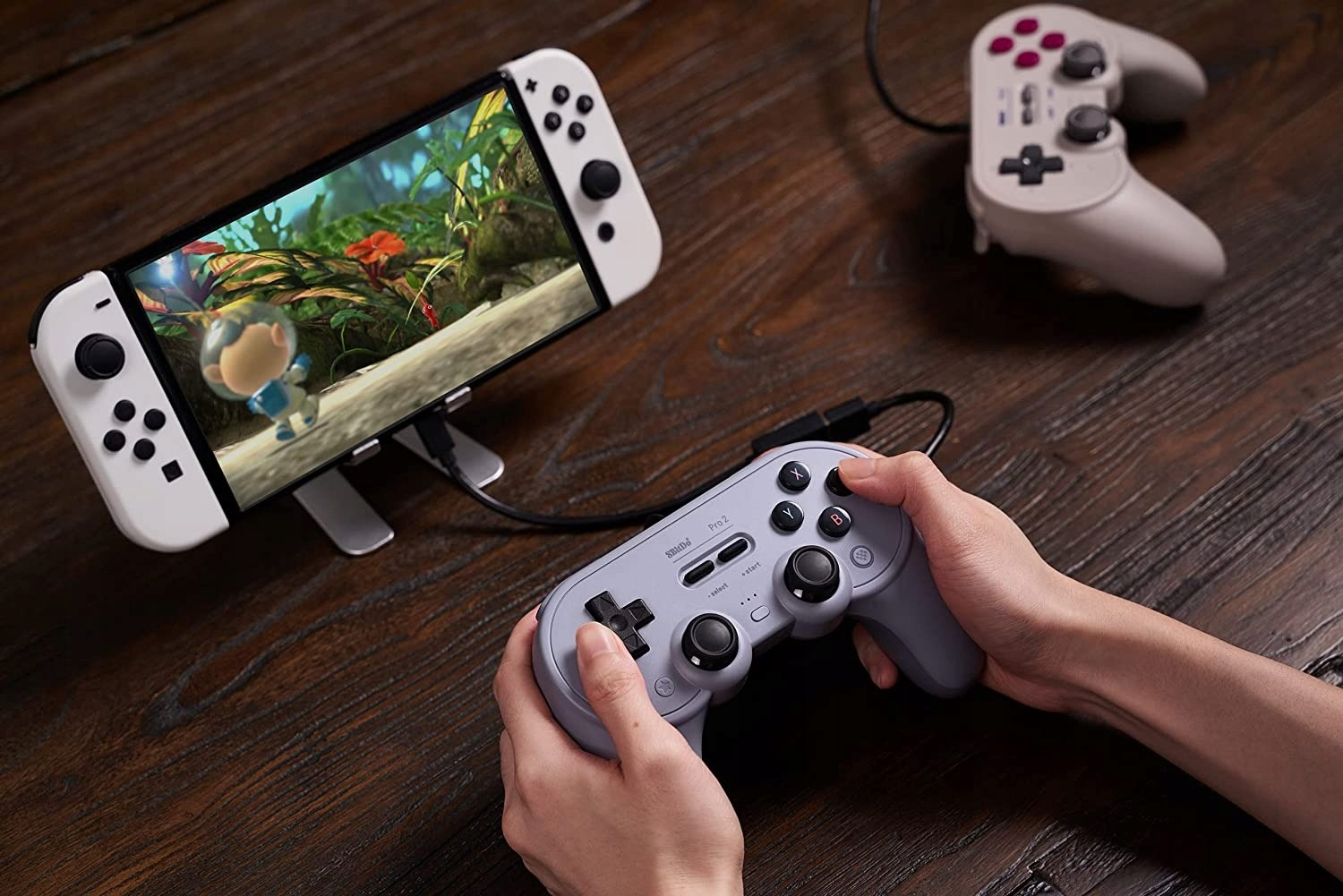 Hände halten grauen Controller, spielen auf Switch. Anderer Controller dahinter.