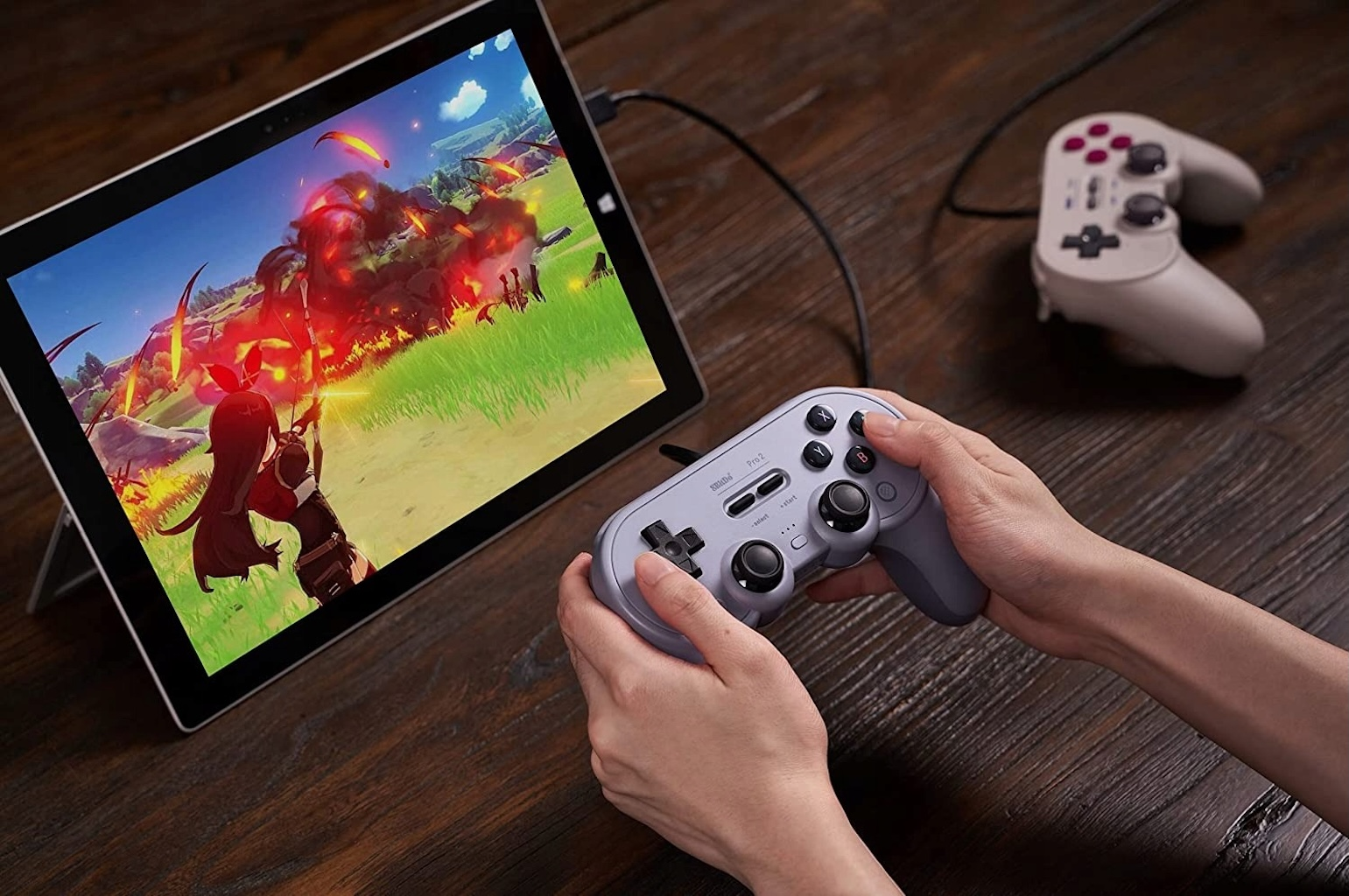 Hände halten grauen Controller, spielen auf Tablet. Controller hinter Tablet.