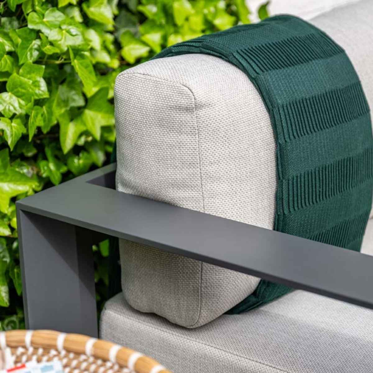 Outdoor sofa with green blanket. Grey frame and foliage in the background.