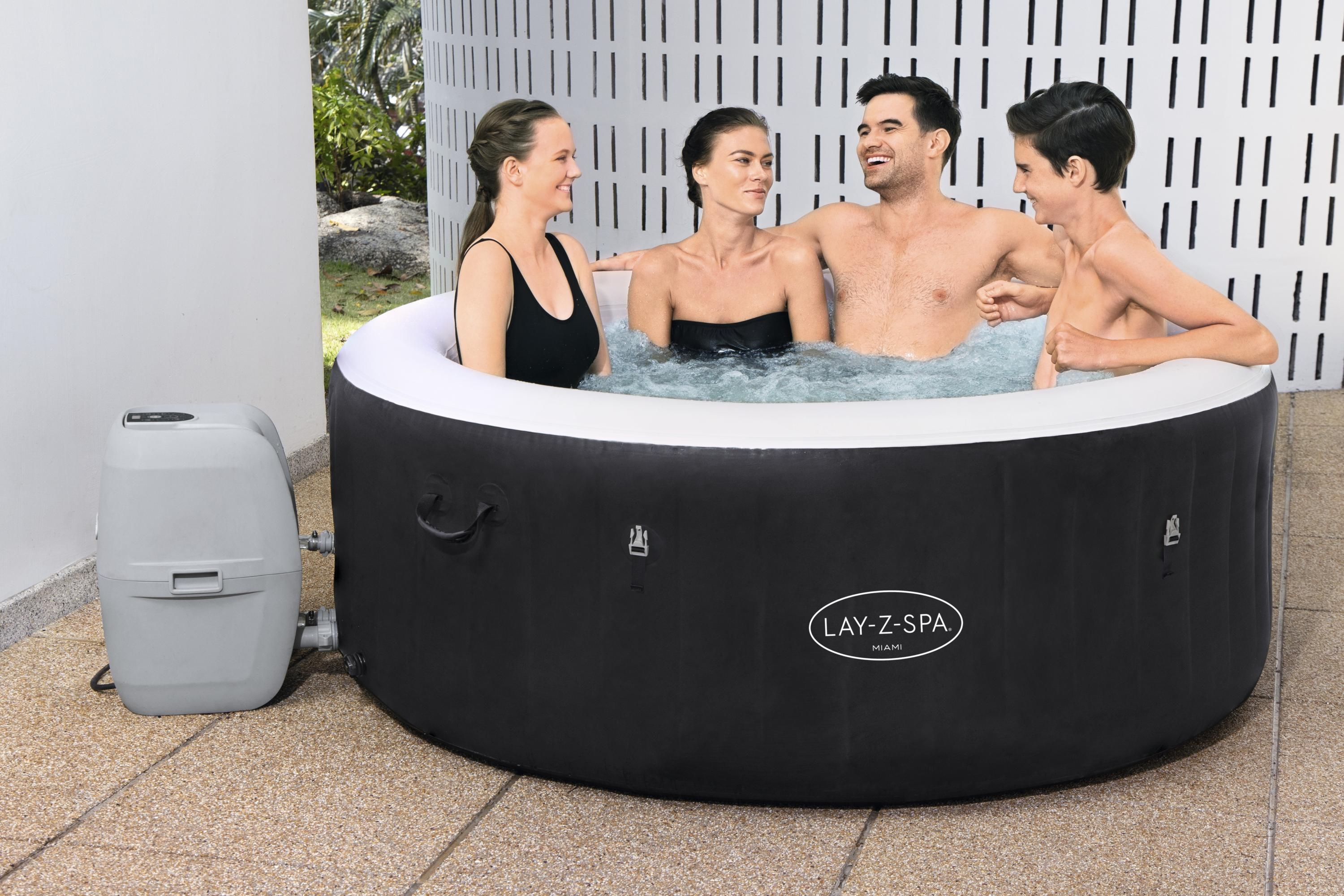 Quattro persone in una vasca idromassaggio bianca e nera, sorridenti. La vasca è su un patio.