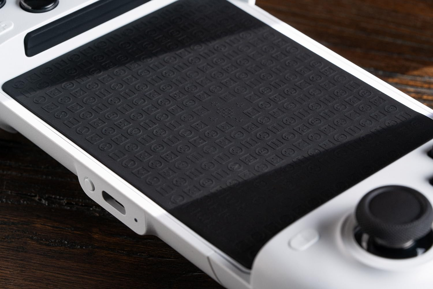 Zbliżenie gamepada z czarną gumową nakładką pośrodku. Biała obudowa.