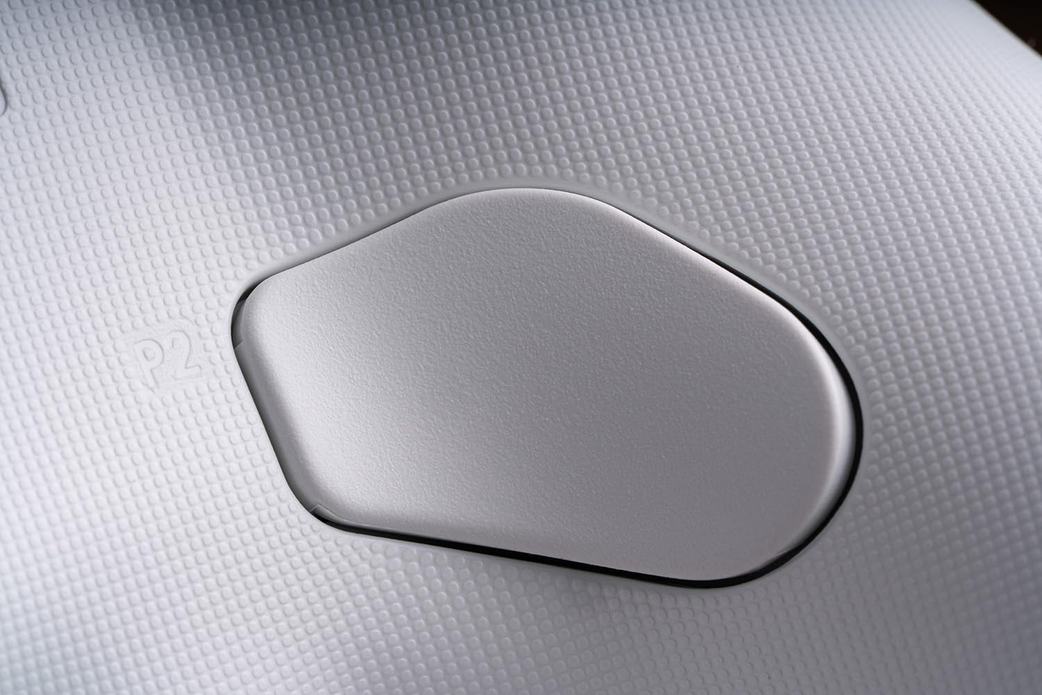 Zbliżenie srebrnego przycisku na białym kontrolerze z kropkowaną teksturą. Przycisk jest zagłębiony.