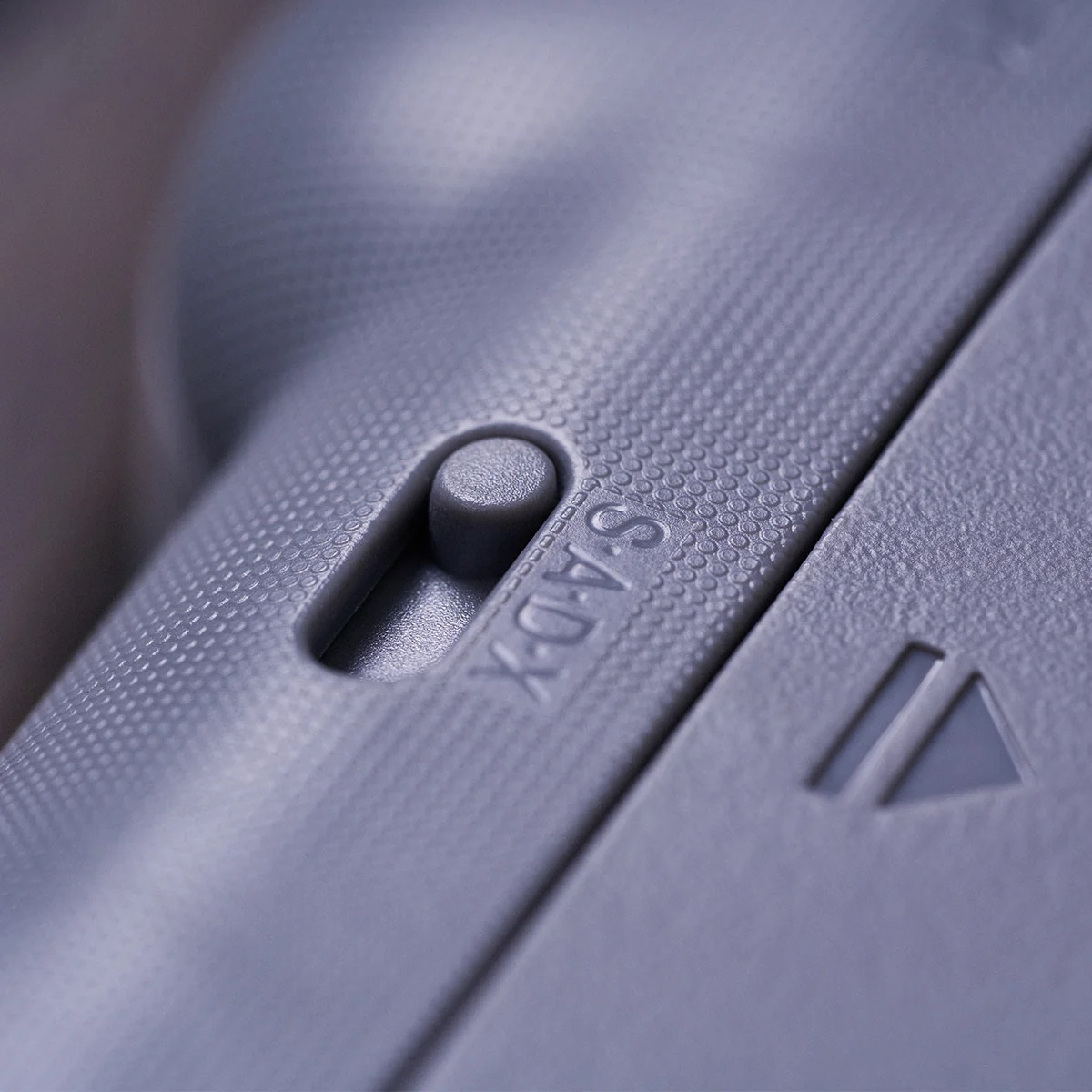 Zbliżenie szarego kontrolera z przełącznikiem z napisem "S.A.D.X" i symbolem trójkąta obok.