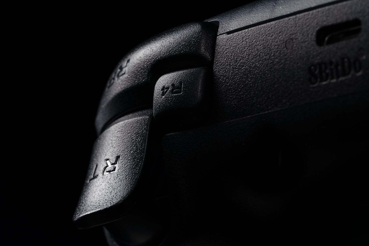 Zbliżenie przycisku spustu czarnego kontrolera, oznaczonego „R4” i „RT”. Ciemne tło.