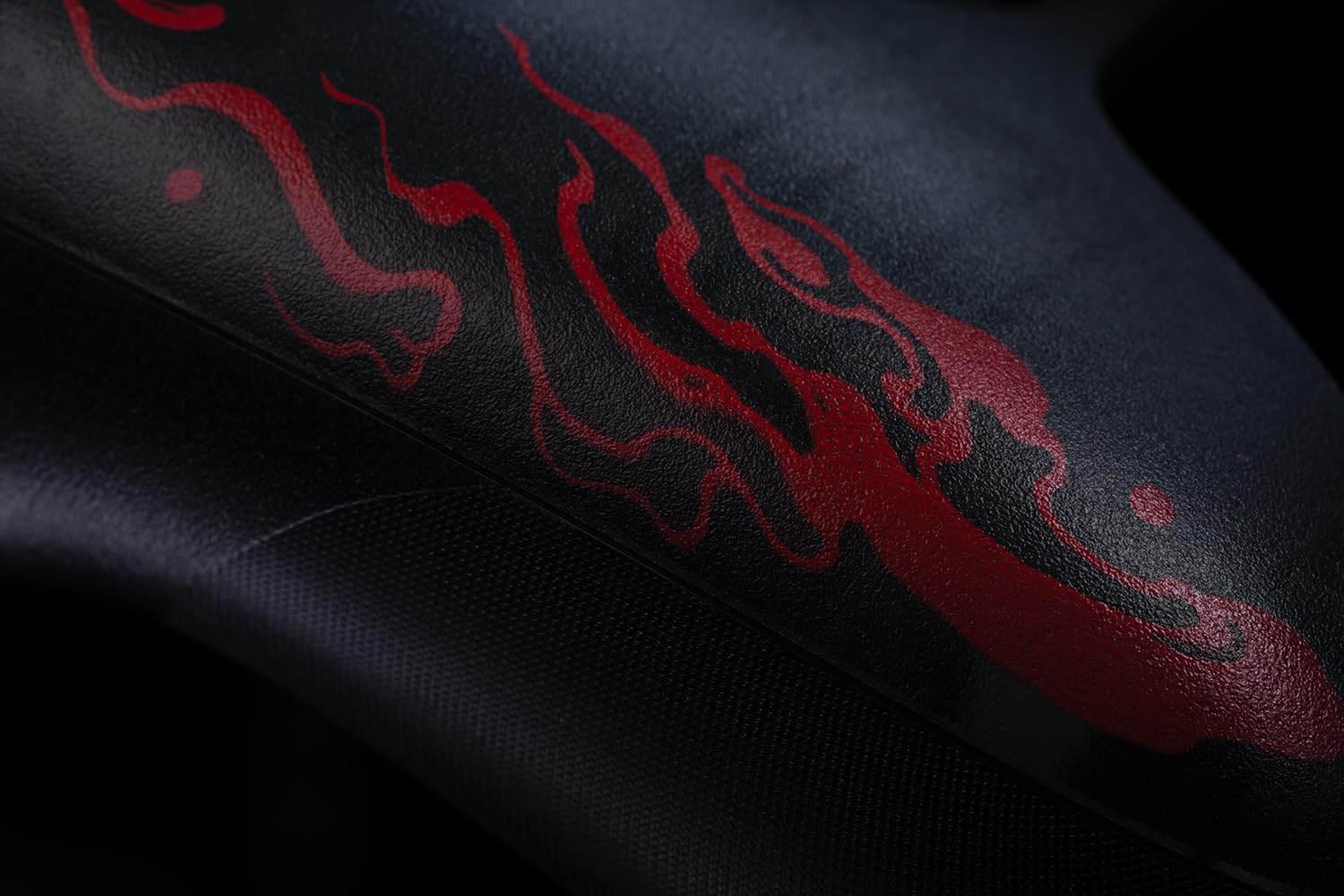 Zbliżenie czarnego kontrolera z czerwonymi wzorami w kształcie płomieni. Czarne tło.