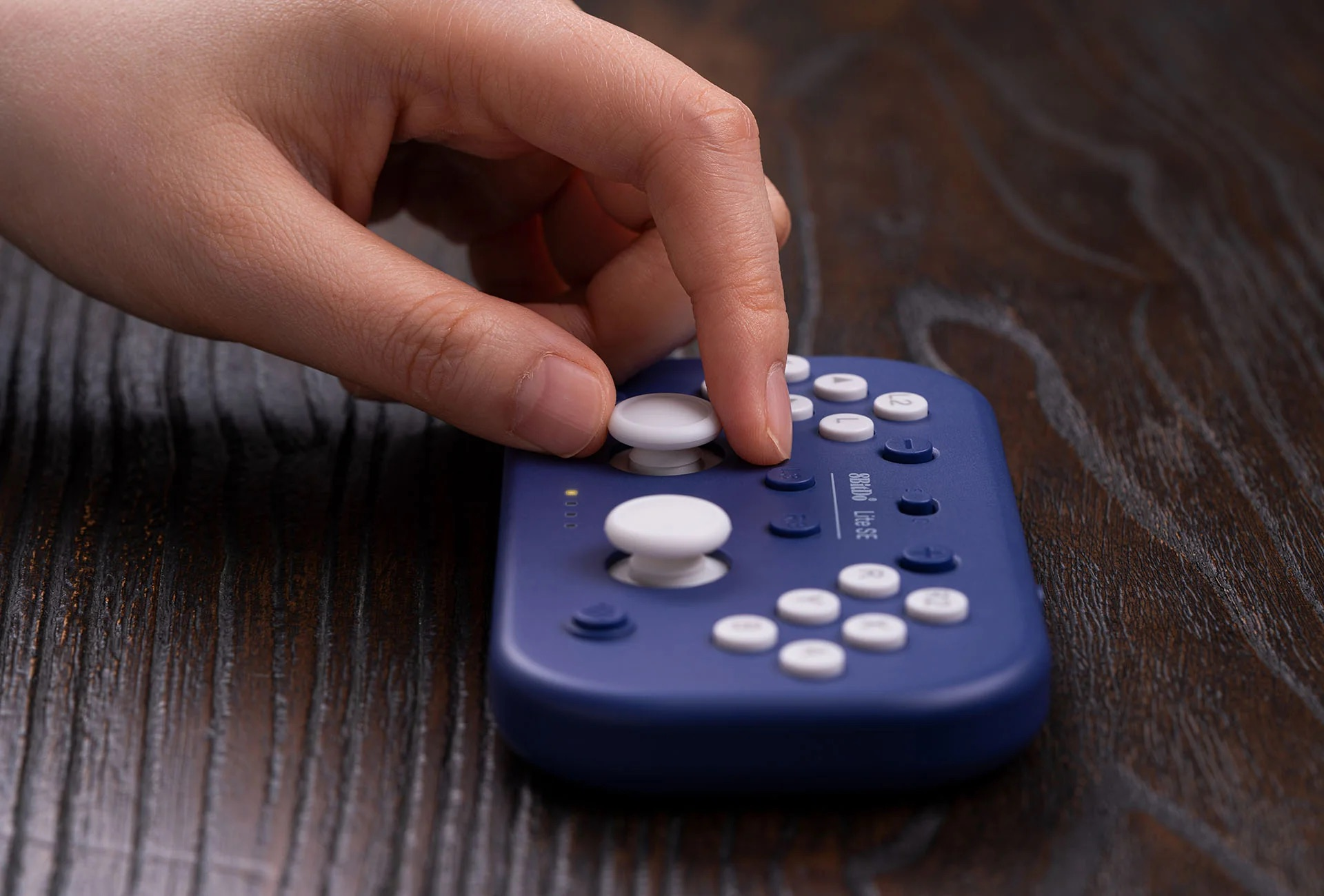 Una mano che posiziona un joystick bianco su un gamepad viola. Lo sfondo è un tavolo di legno.