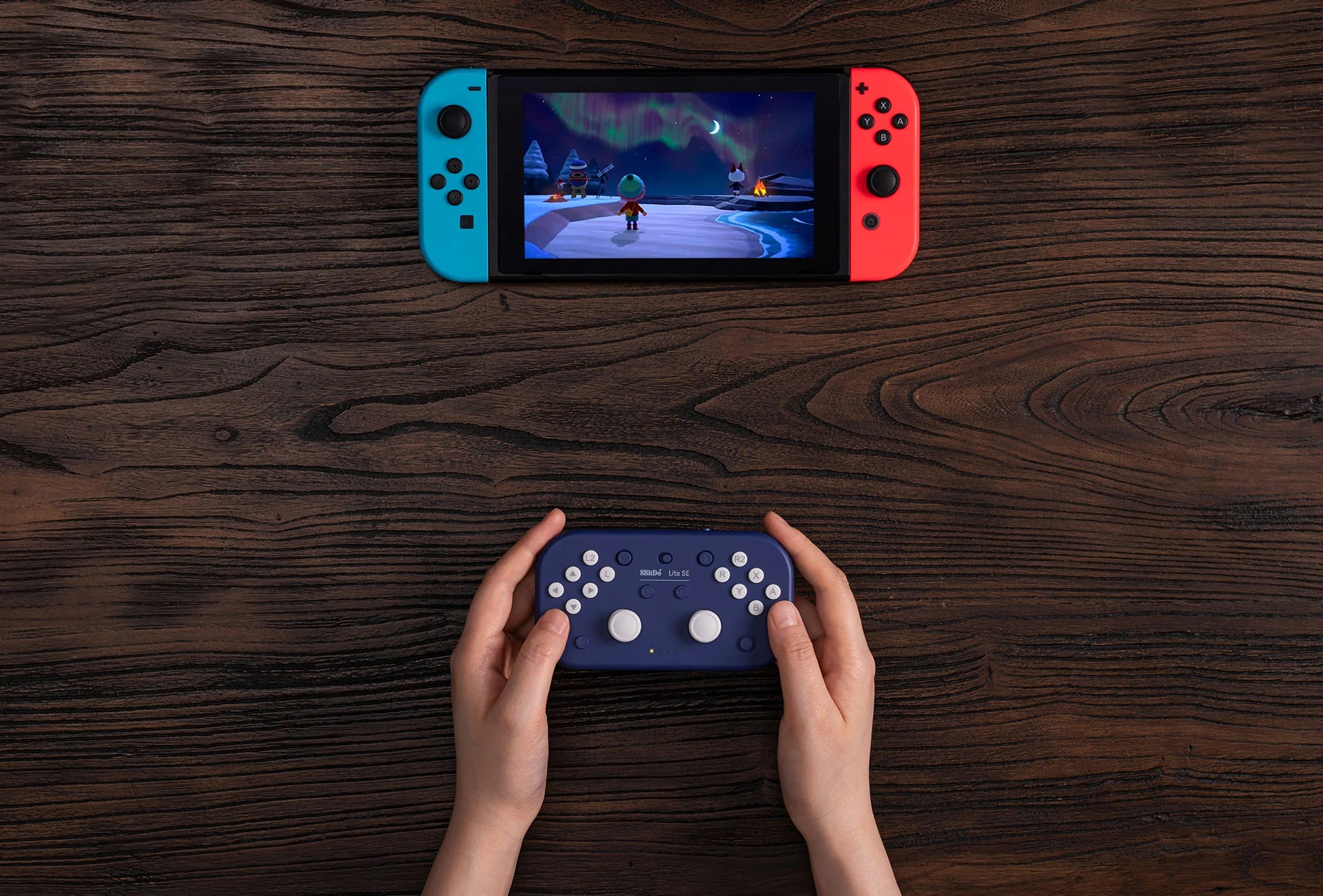 Le mani di una persona che tengono un gamepad blu e una Nintendo Switch. Sono su un tavolo di legno.