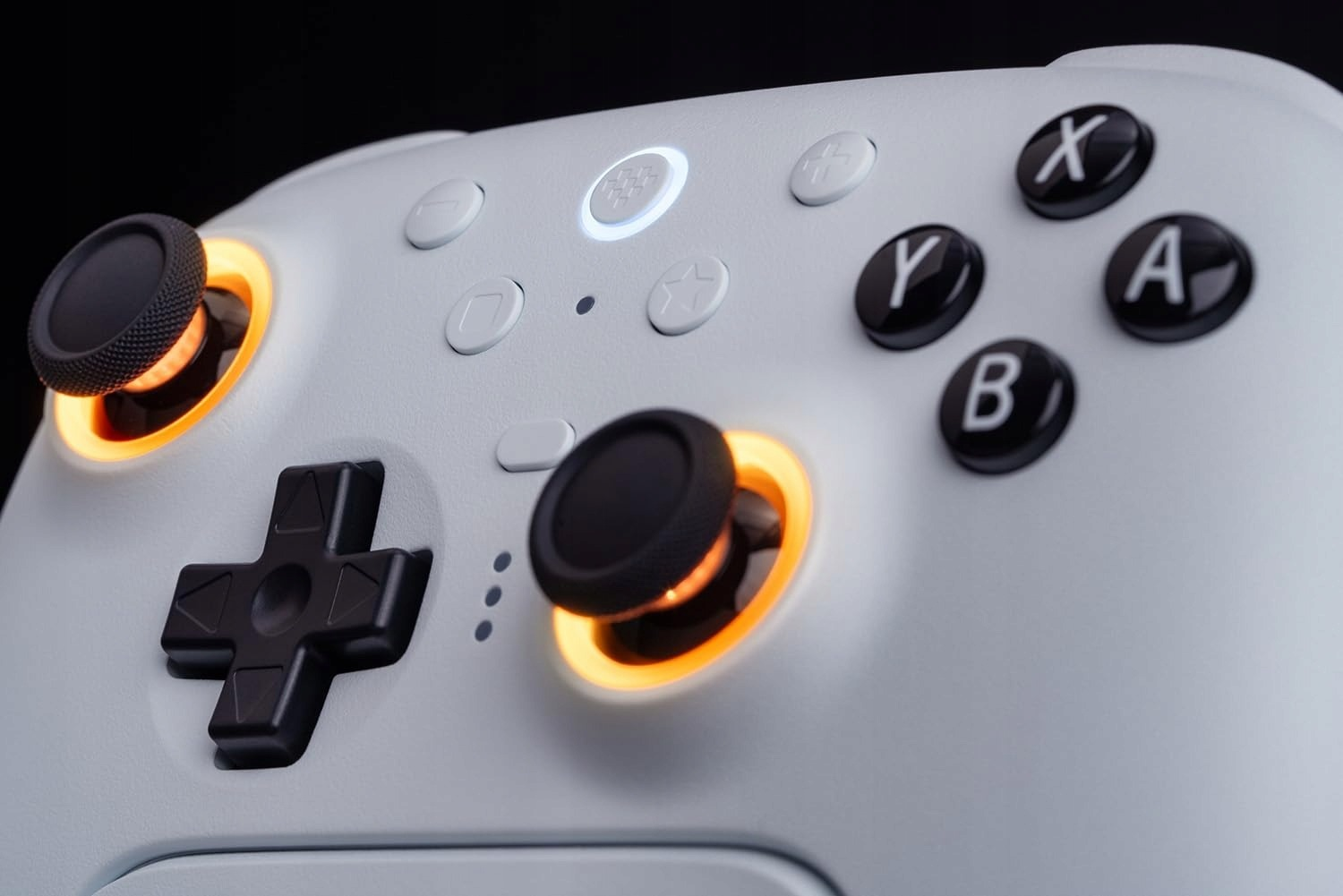 Zbliżenie białego gamepada z podświetlanymi joystickami. Posiada przyciski X, Y, A, B i krzyżak.