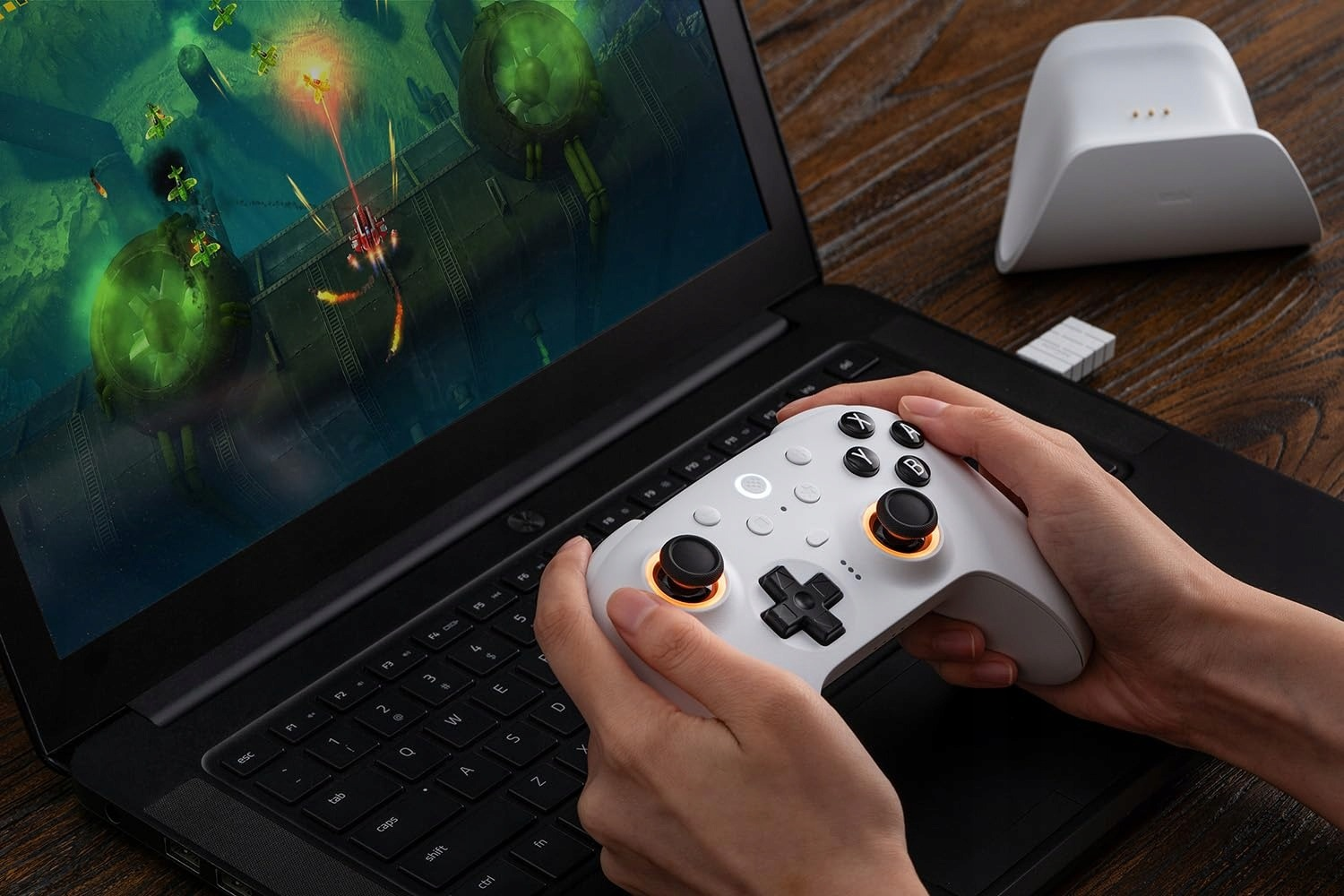 Osoba gra w grę na laptopie, trzymając biały kontroler do gier.
