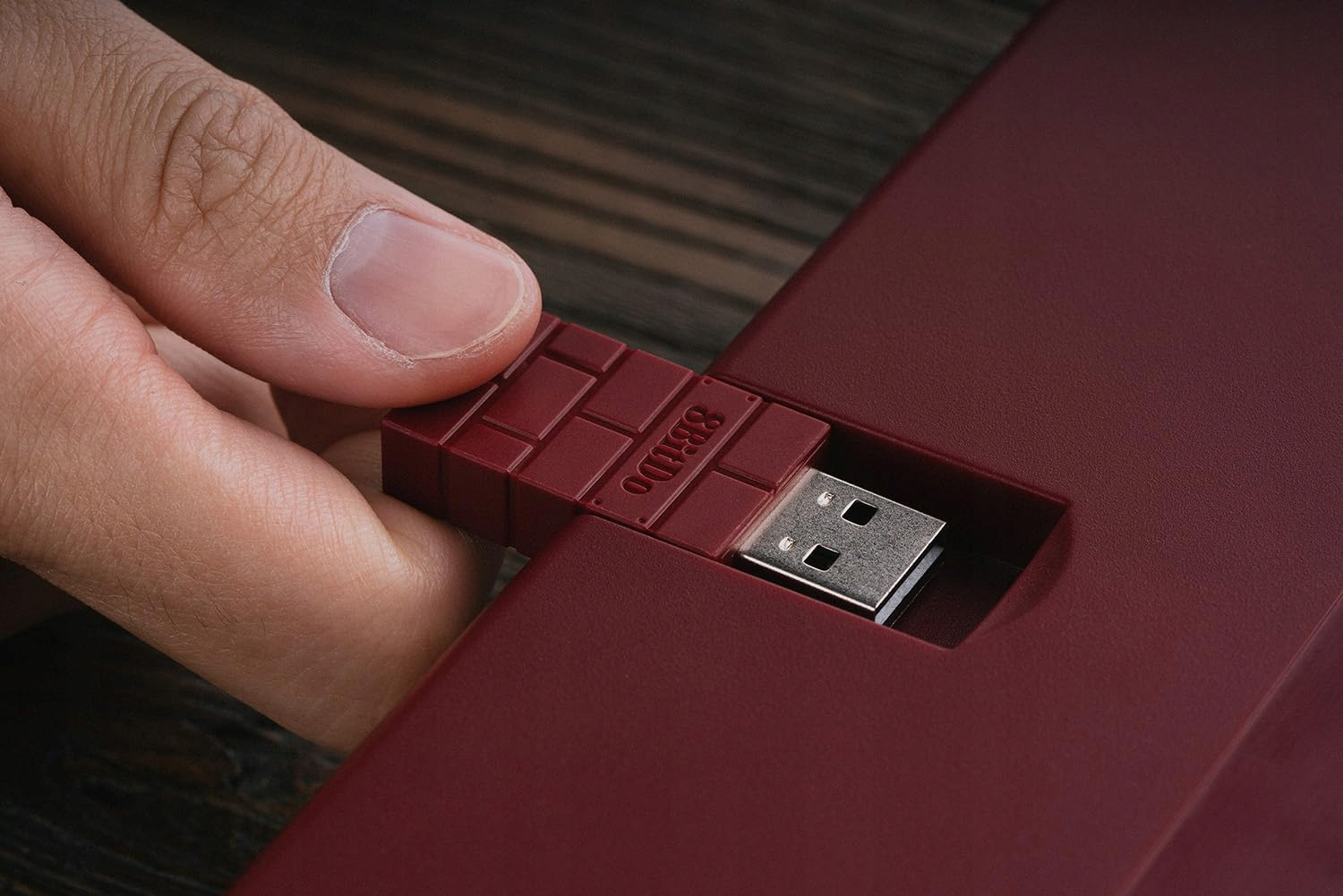 Ręka wkładająca odbiornik USB do bordowego gniazda w kształcie cegły. Tło również jest bordowe.