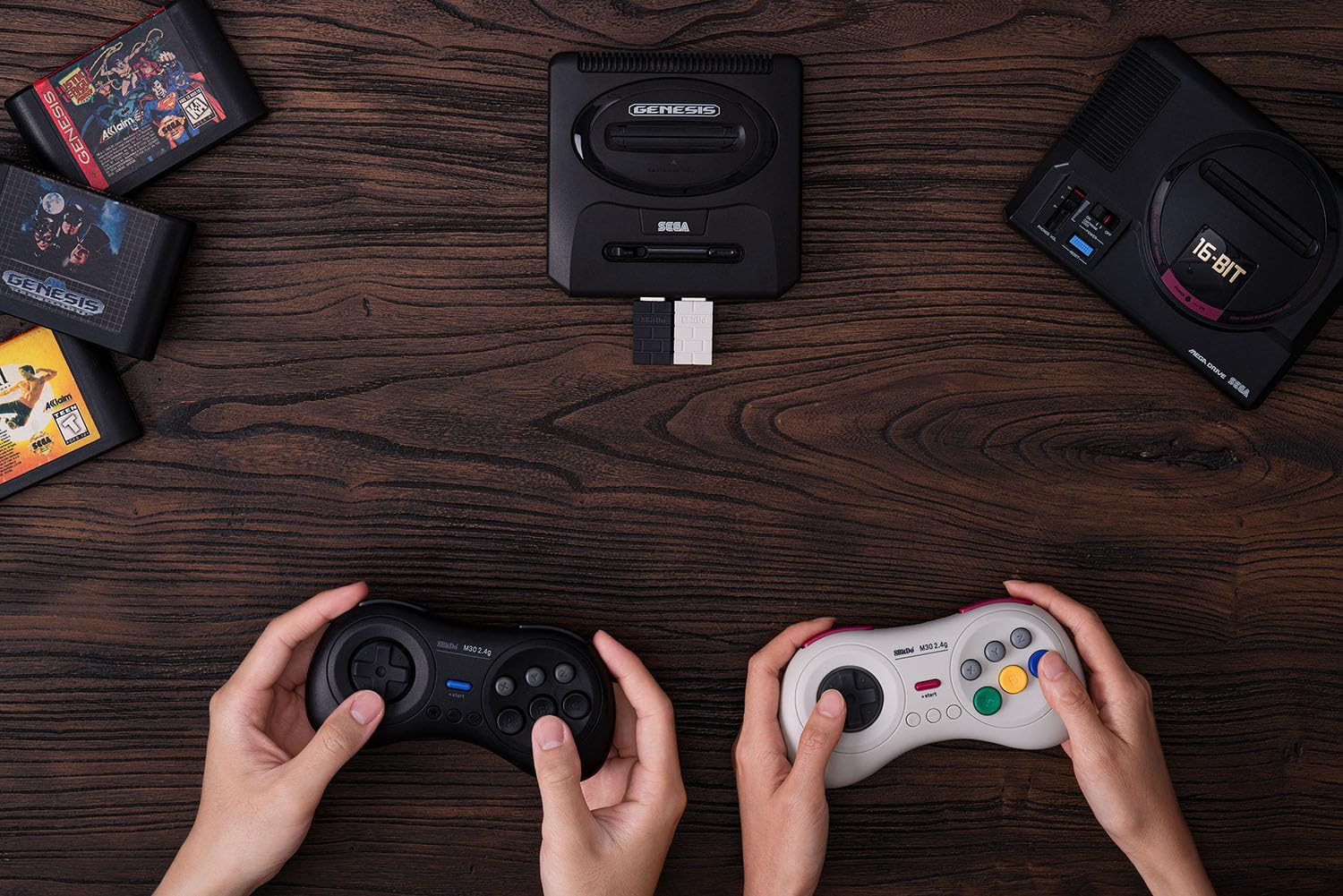 Due mani tengono controller. Due console Sega Genesis e cartucce su un tavolo di legno.