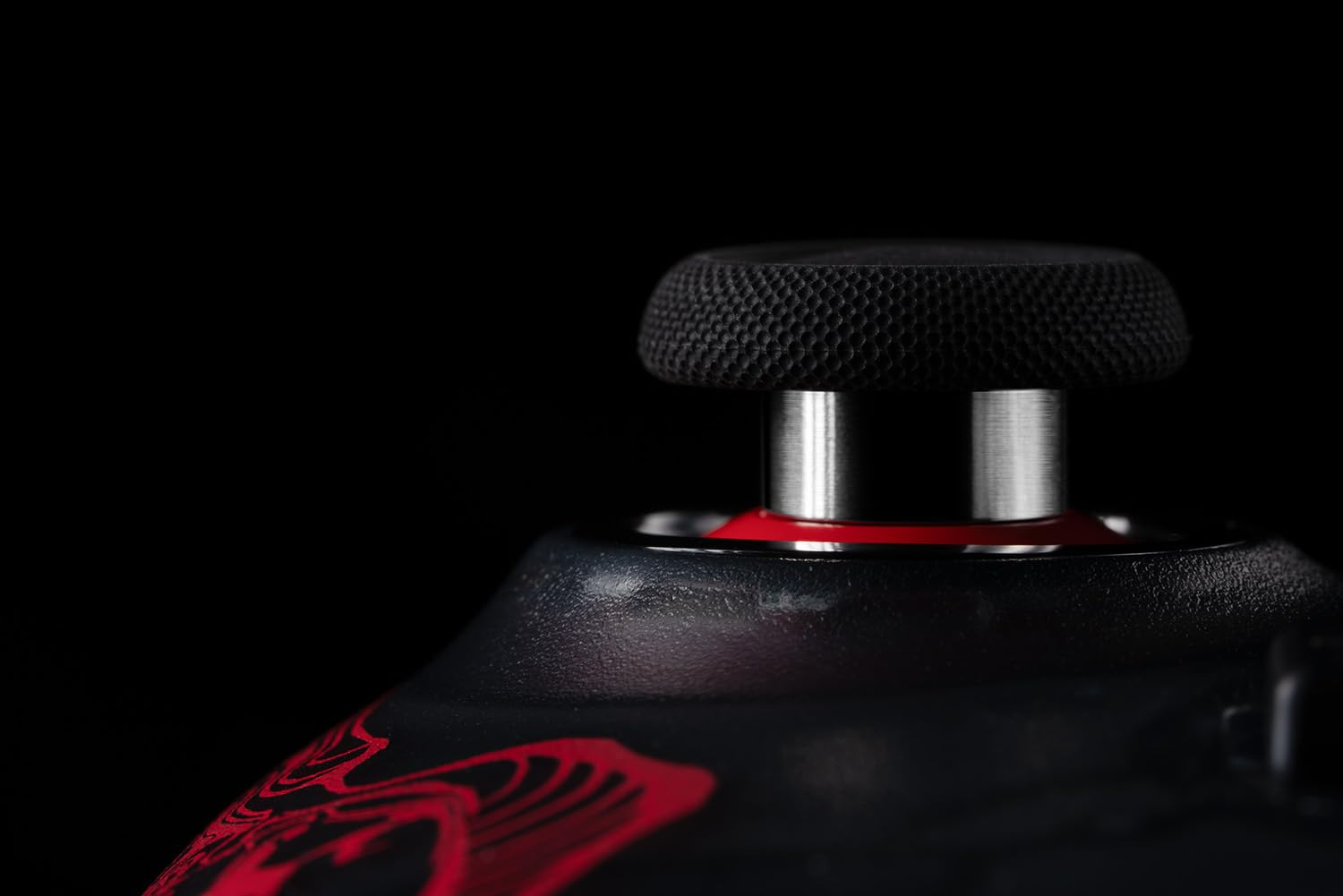 Zbliżenie czarnego joysticka z teksturowanym wierzchem, na czarnym tle z czerwonymi akcentami.