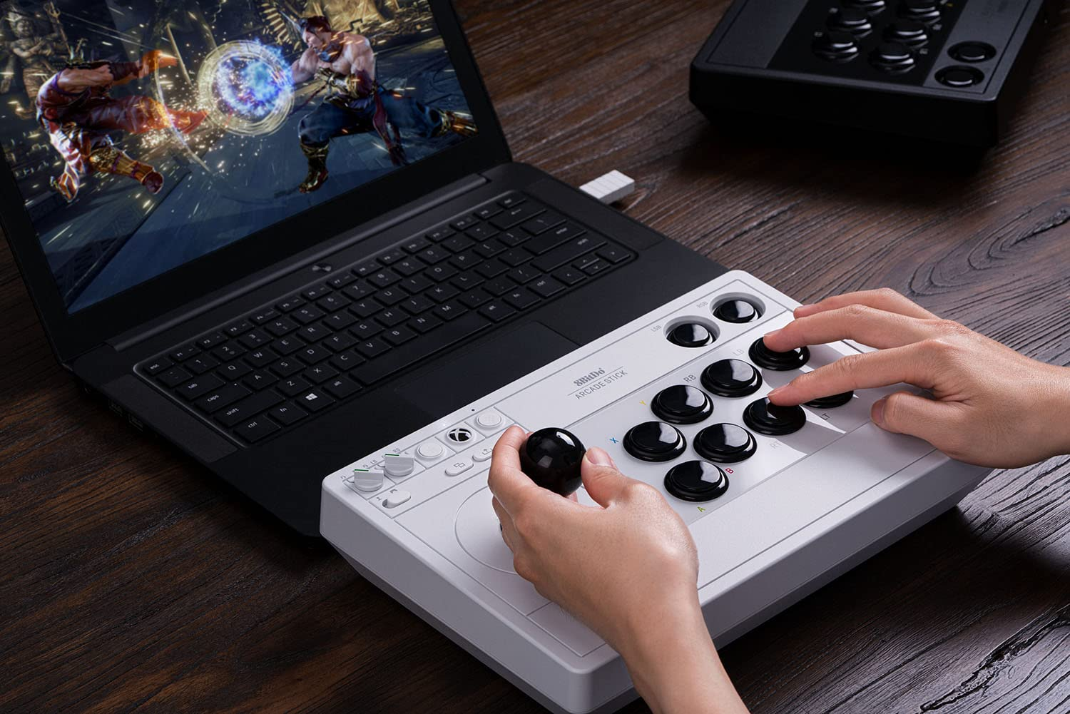 Osoba korzystająca z joysticka arcade podłączonego do laptopa. Ekran pokazuje grę walki.