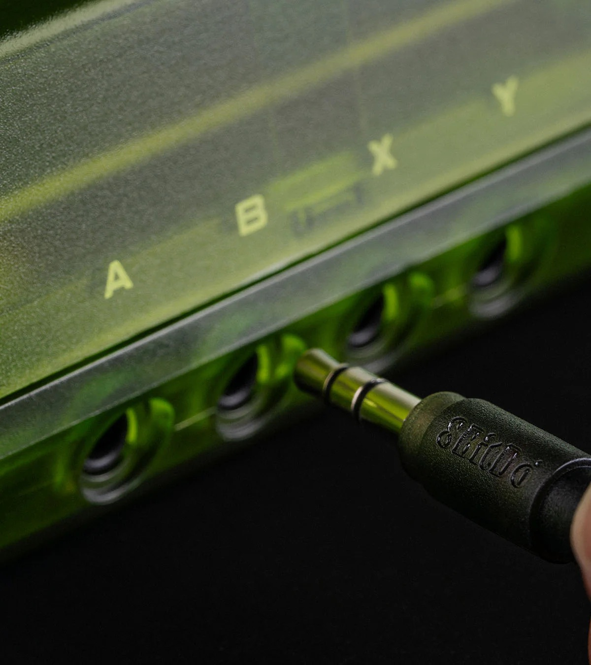 Primo piano di un dispositivo verde a cui si sta collegando un jack per cuffie. Una mano tiene il jack.