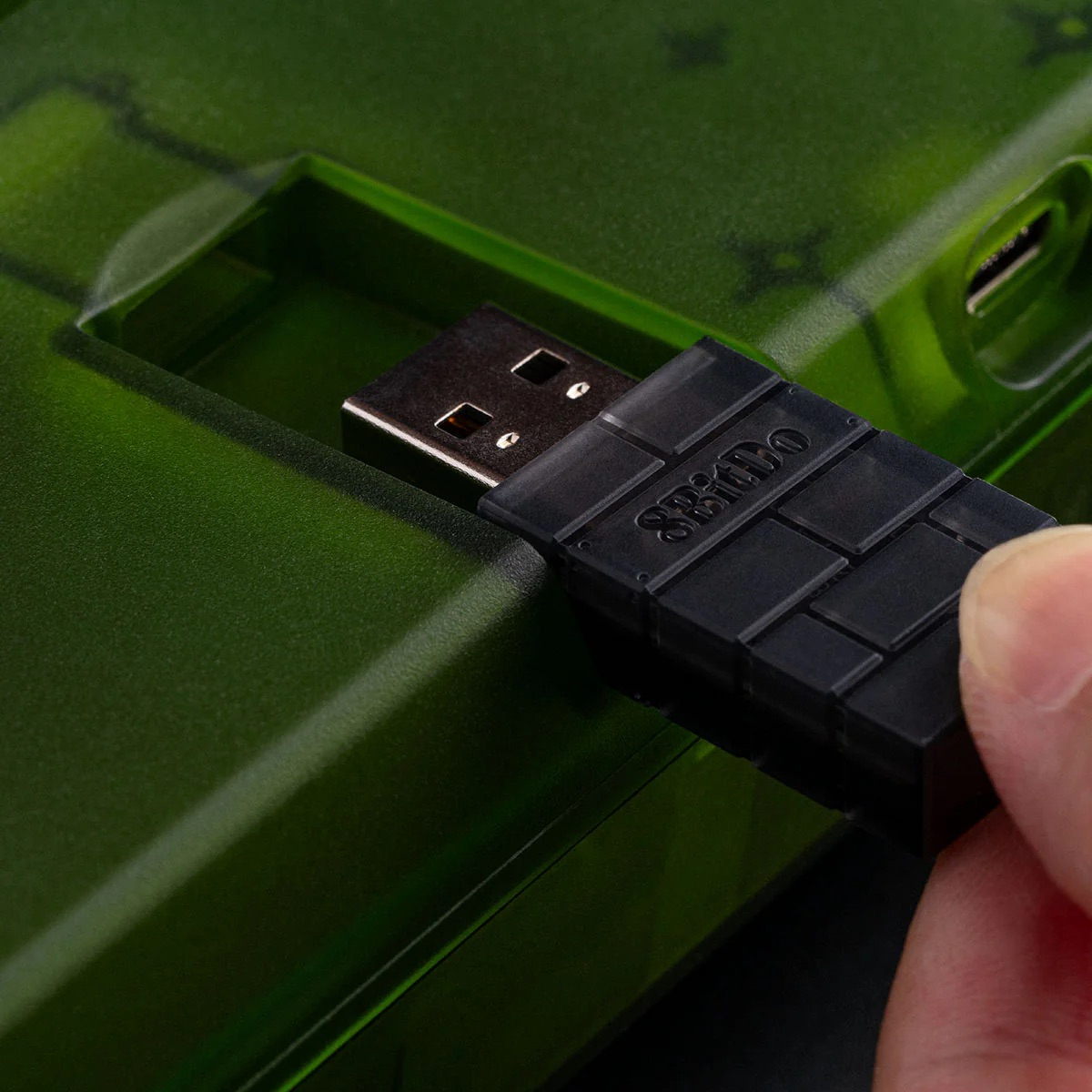 Una mano che inserisce un ricevitore USB in una tastiera verde.