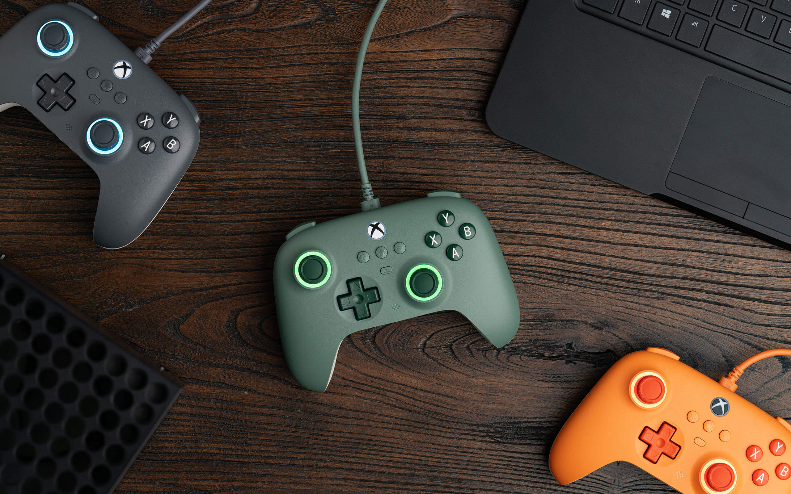 Vista dall'alto di tre controller di gioco, verde, arancione e grigio, su una superficie di legno.