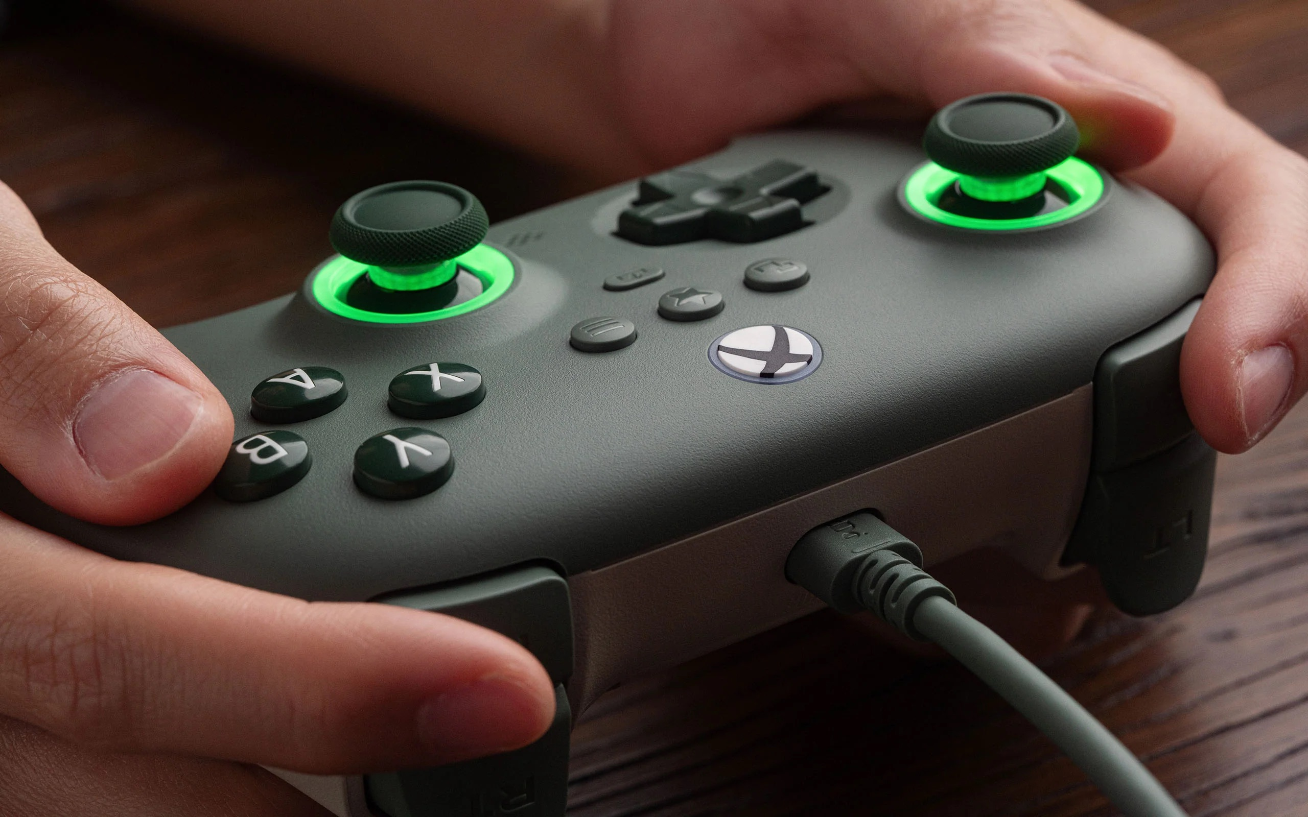 Mani che tengono un controller di gioco verde con joystick e pulsanti luminosi.