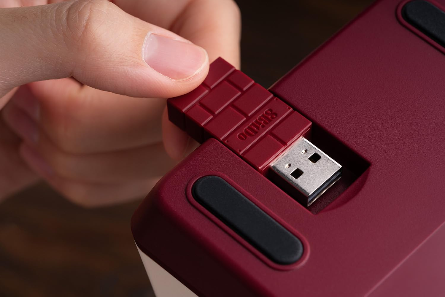 Ręka wkładająca USB w kształcie cegły do bordowej klawiatury.