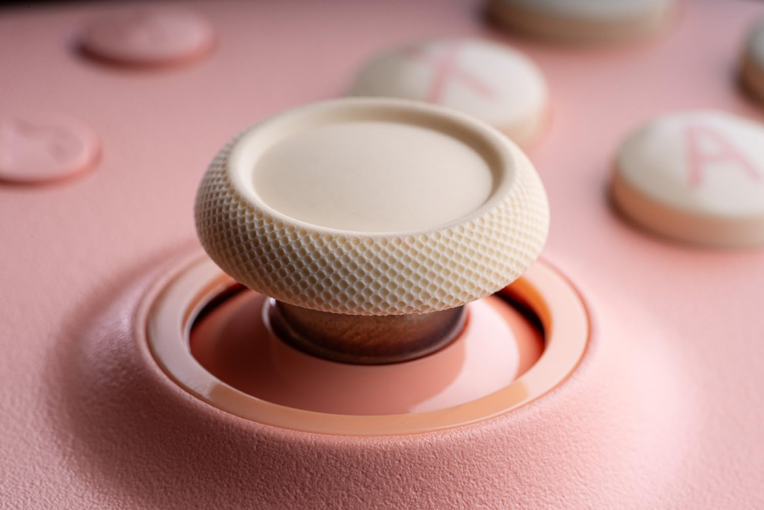 Zbliżenie kremowego dżojstika otoczonego różową podstawą na różowym kontrolerze 8bitdo.