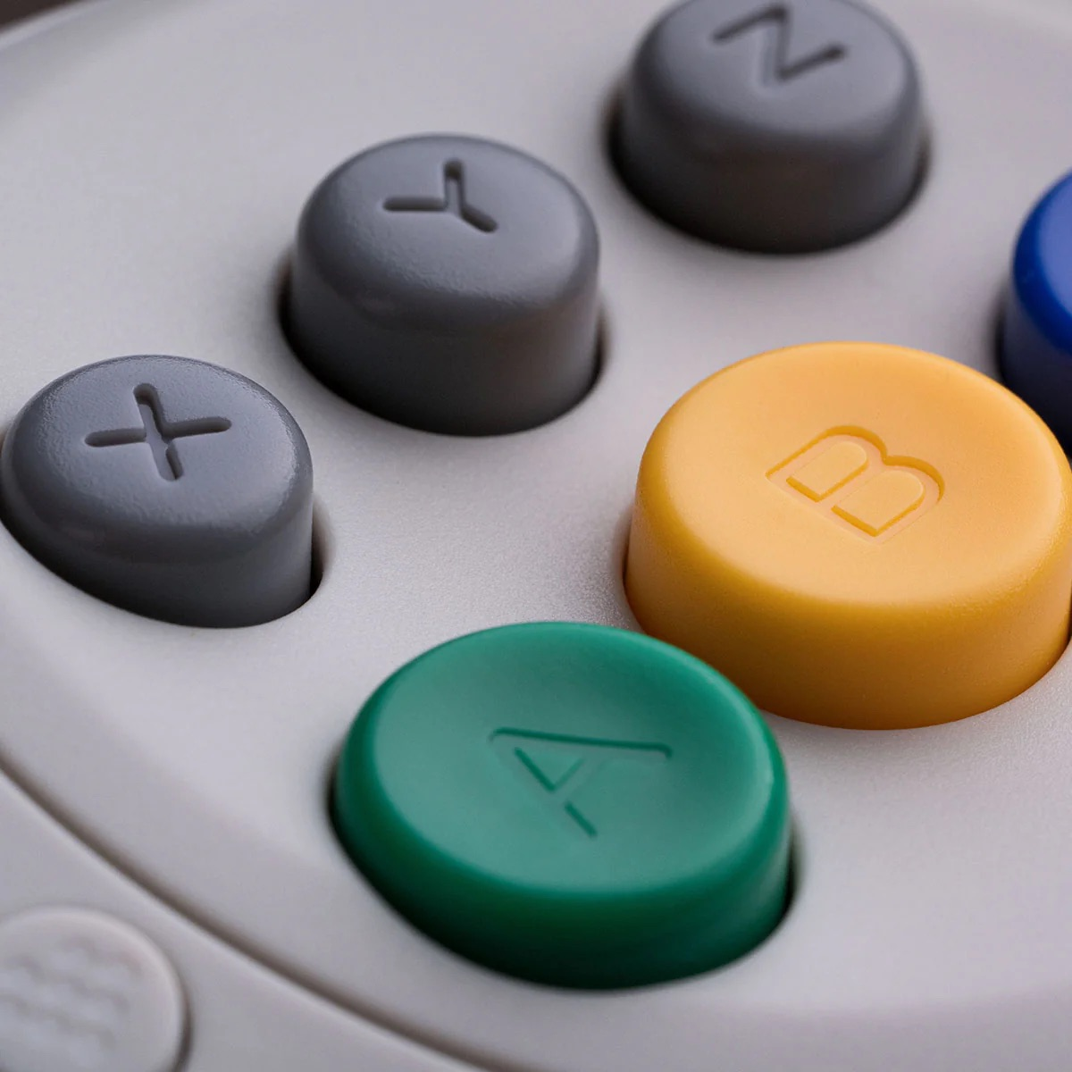 Zbliżenie kolorowych przycisków. Zielony A, żółty B i szare przyciski są widoczne.